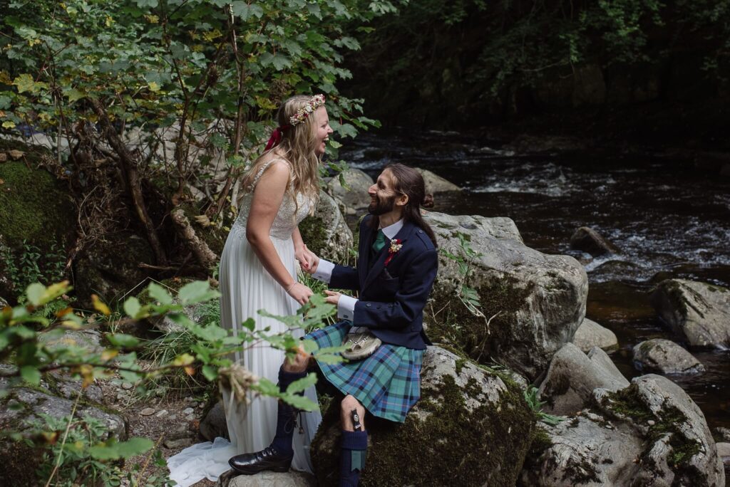 elopement couple by waterfall on wedding day in wedding dress and kilt laughing
