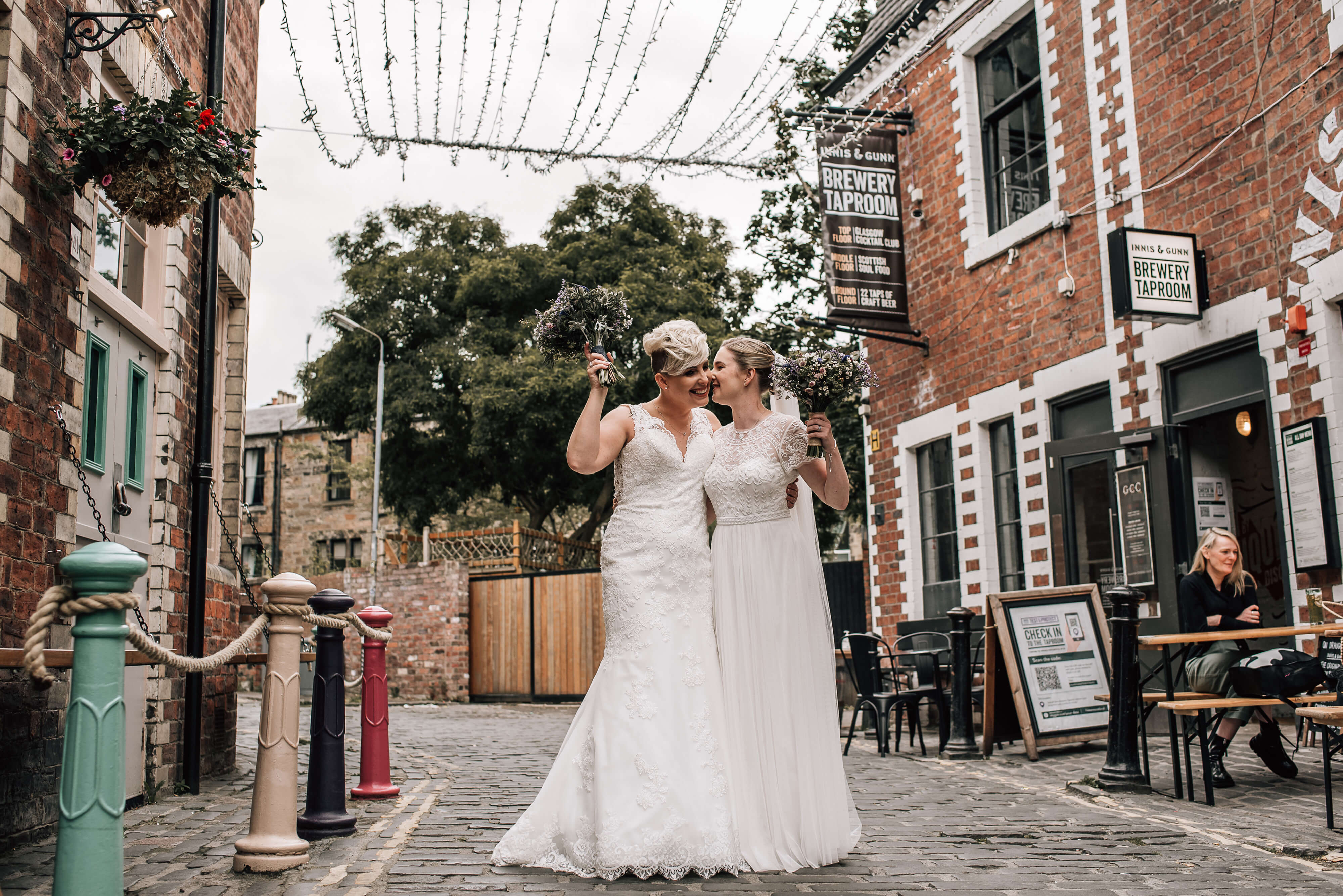 two smiling brides on a cobbled street in wedding dresses alternative wedding photographer scotland