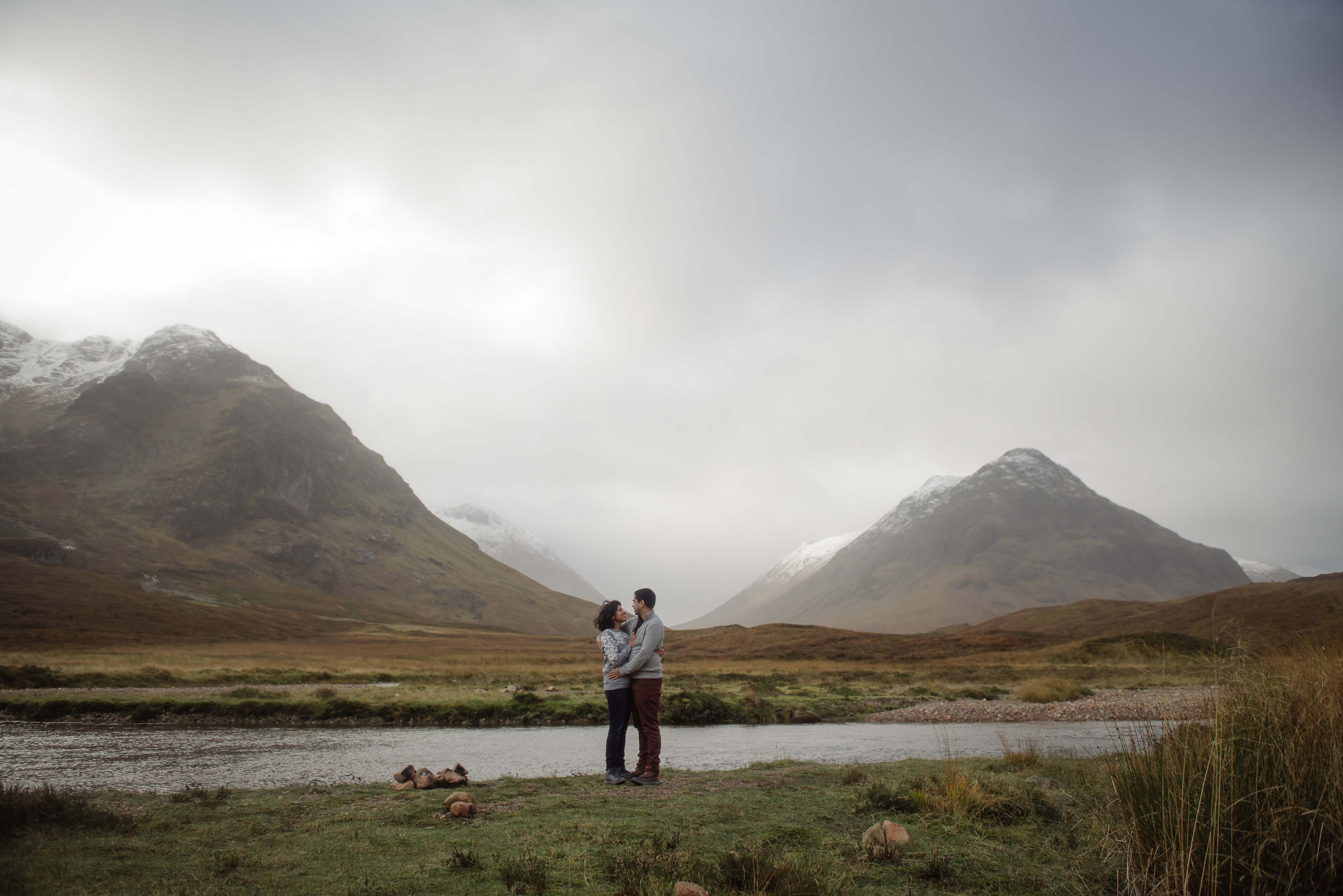 couple in front of mountains of glencoe scotland after getting engaged