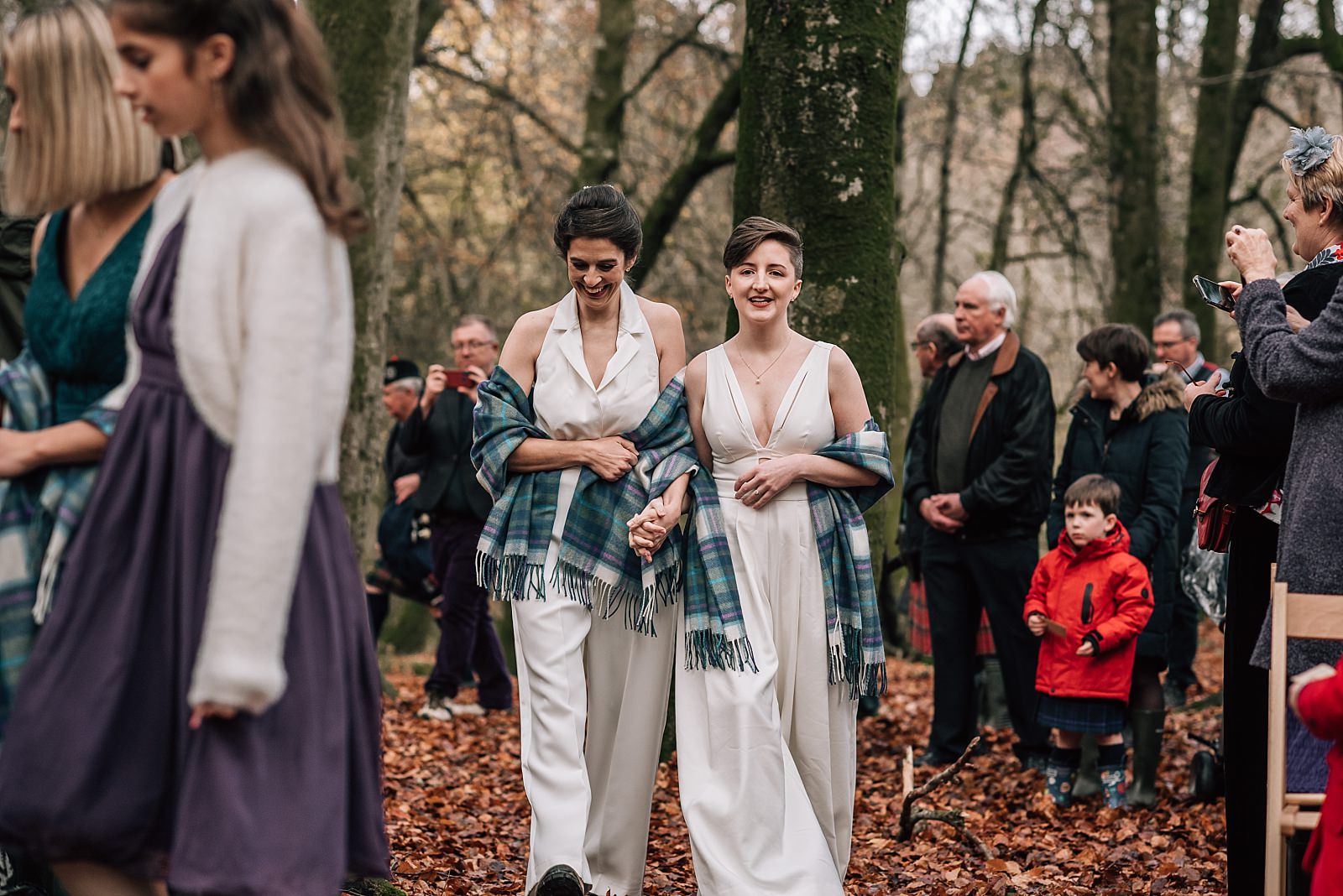 two brides walking through the woods up the aisle at their boreland loch tay wedding day with outdoor ceremony