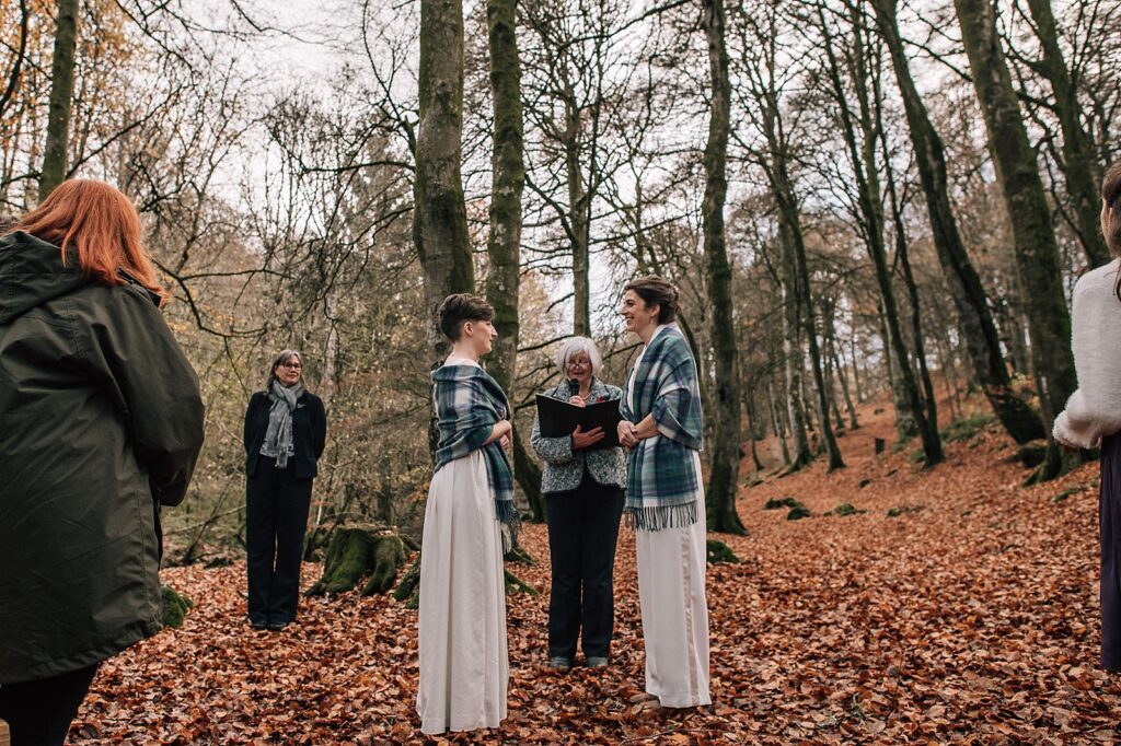 two brides standing with tartan shawls on at their outdoor ceremony in the woods at their boreland loch tay wedding