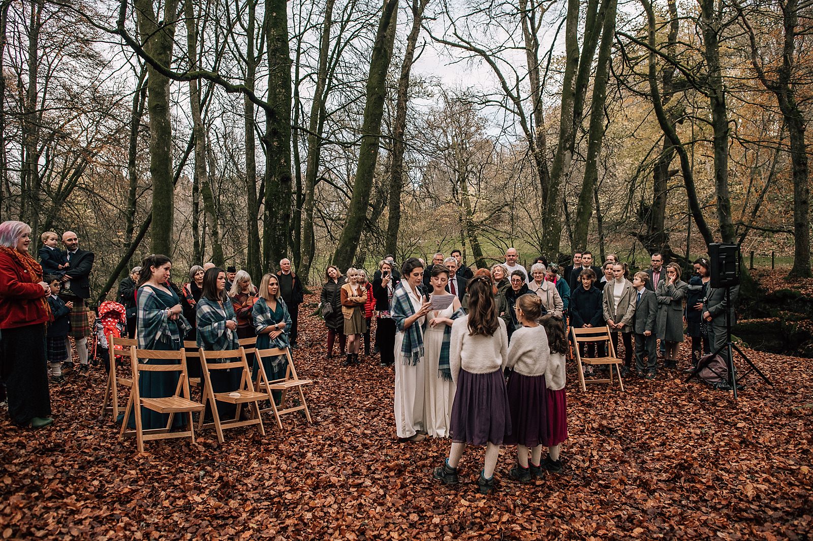 two brides standing with tartan shawls on at their outdoor ceremony in the woods at their boreland loch tay wedding