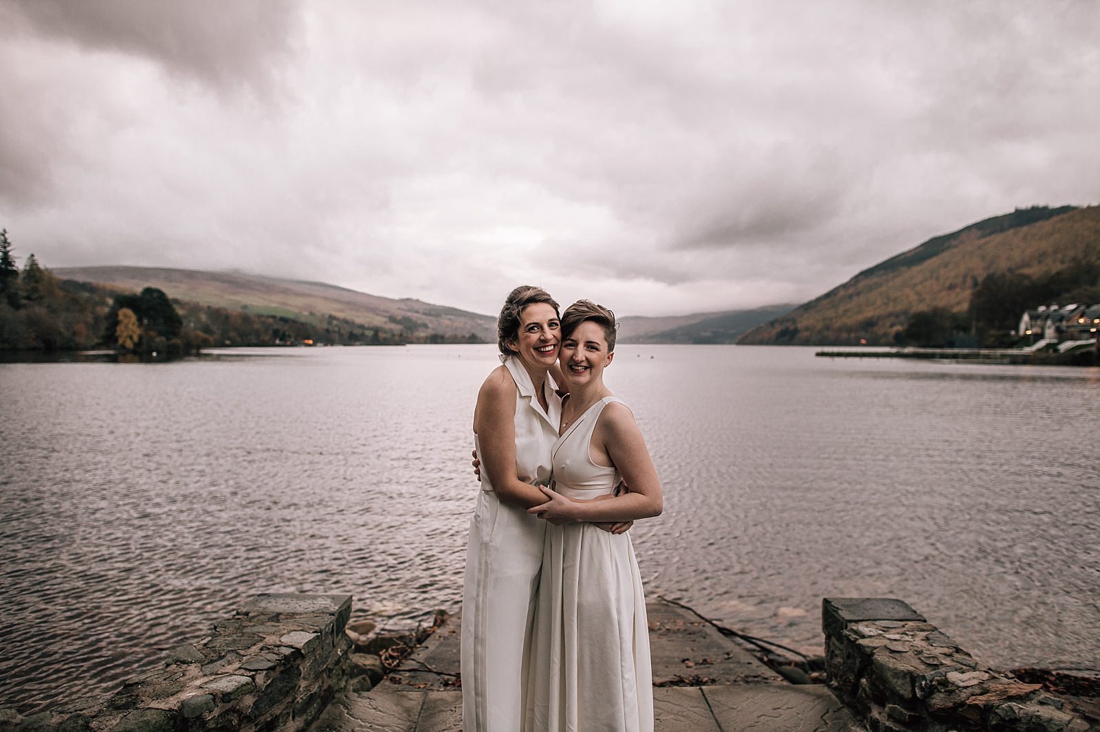 two brides smiling on the shores of loch tay on their wedding day in perthshire scotland