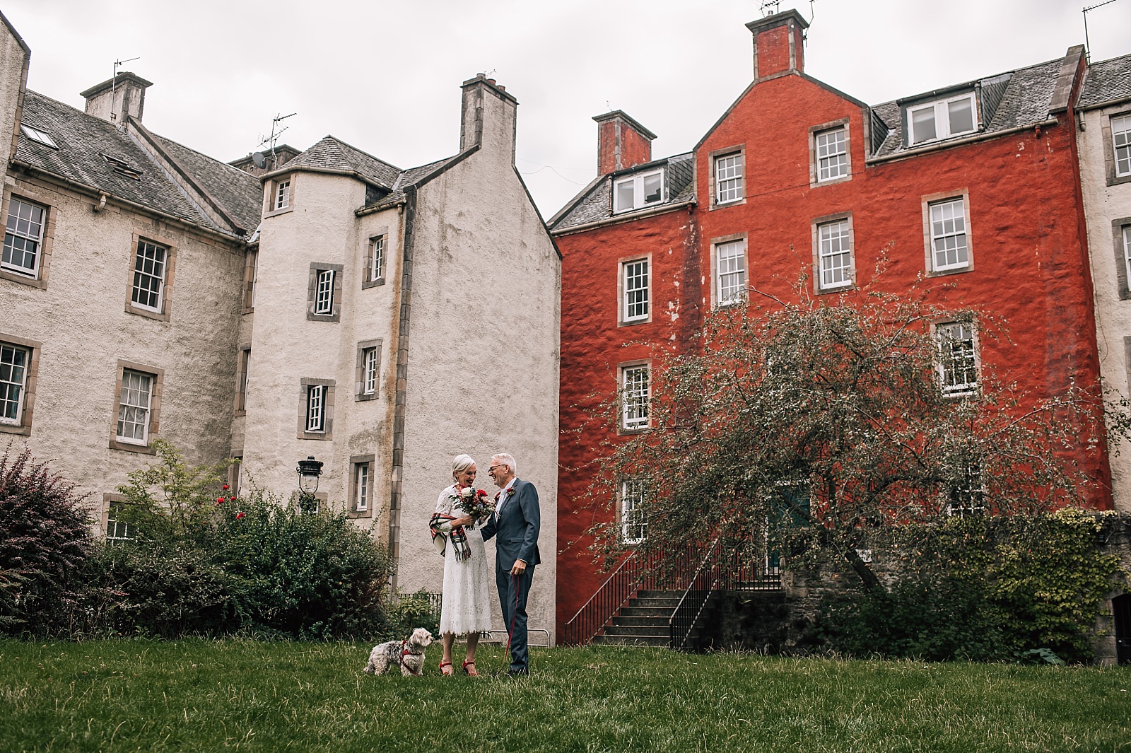 mature couple and rescue dog pose for photos on their wedding day by elopement photographer edinburgh in front of red house
