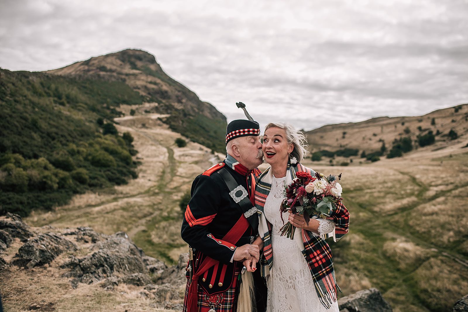 scottish piper kisses bride on her wedding day in edinburgh scotland at top of arthurs seat