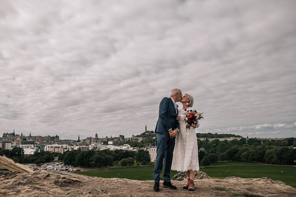 mature bride and groom kiss on the elopement wedding day with edinburgh city centre in the background