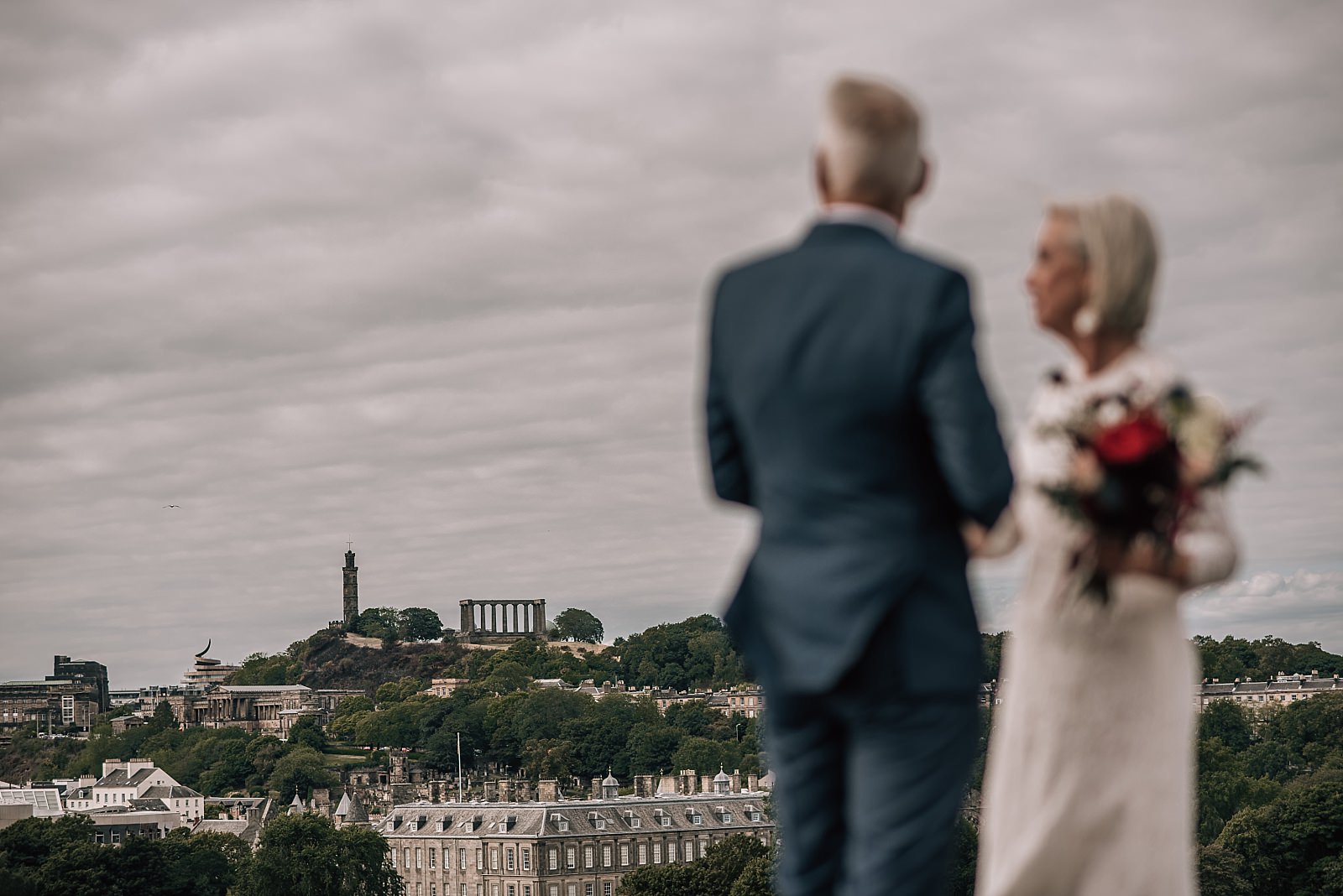mature bride and groom on the elopement wedding day look out with edinburgh city centre in the background