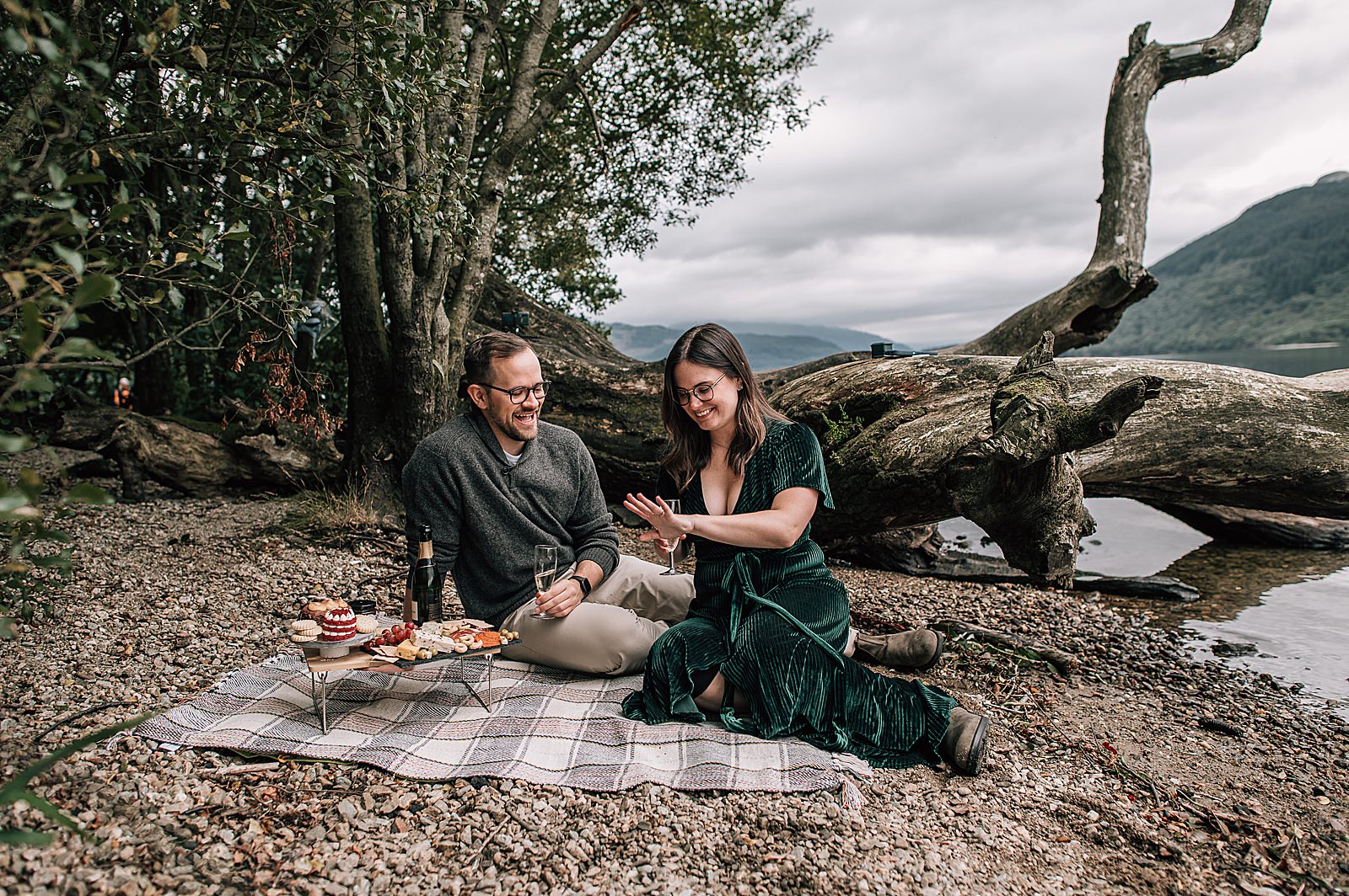 couple sitting on picnic blanket on private beach at Loch Lomond after surprise proposal photos shot by proposal photographer scotland