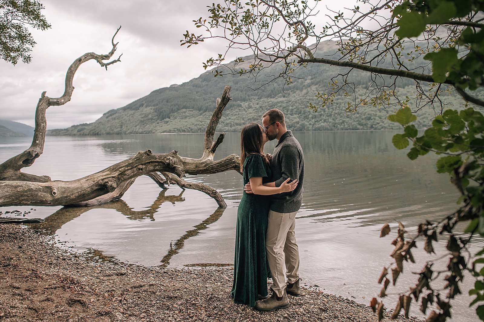 newly engaged couple kissing on the shores of Loch Lomond after proposal shot by engagement photography scotland