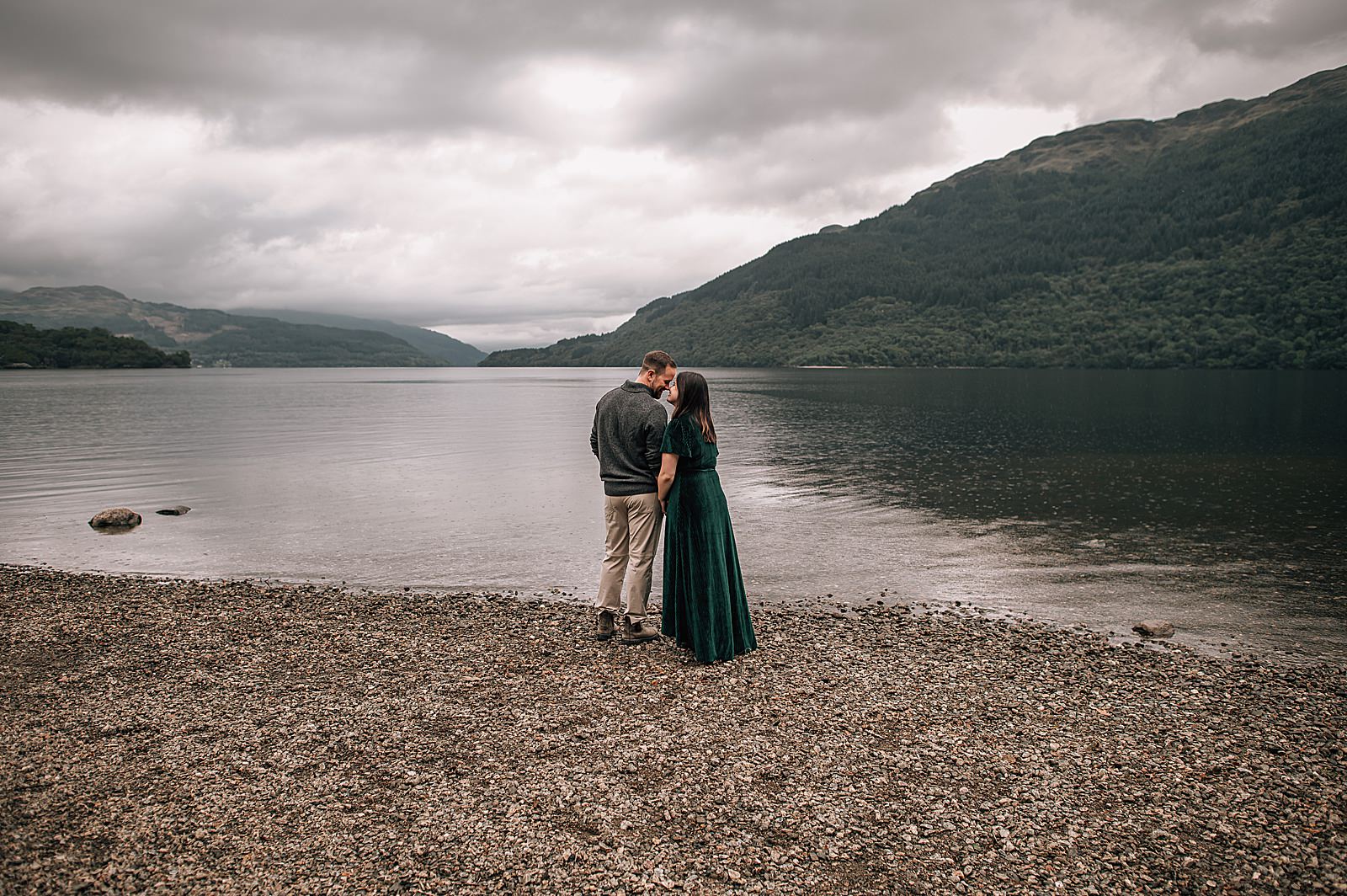 couple standing on pebble beach at Loch Lomond scotland after surprise proposal glasgow shot by proposal photographer scotland