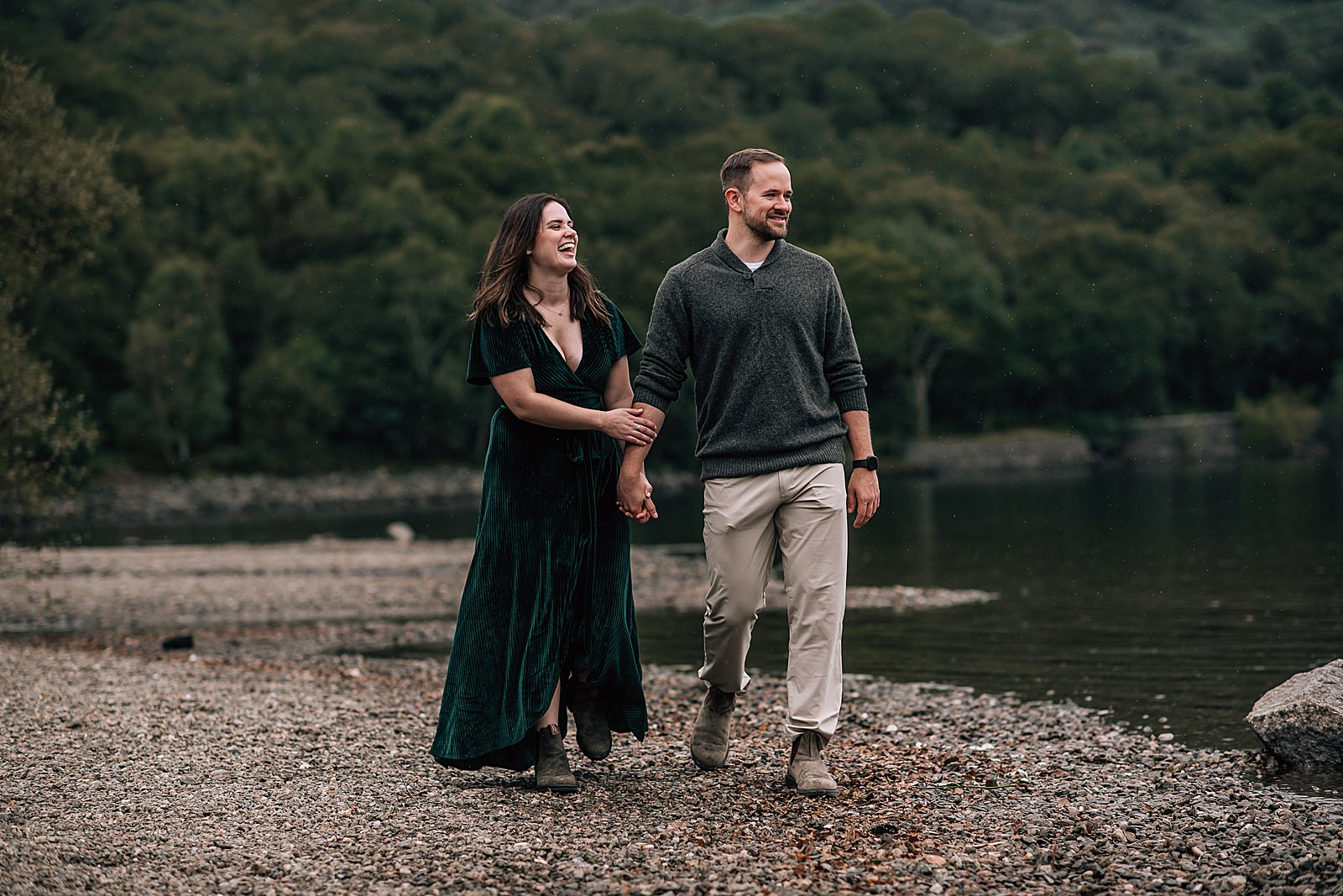 newly engaged couple smiling and laughing as they walk along the shore of Loch Lomond after their surprise proposal photo shoot scotland by proposal photographer scotland