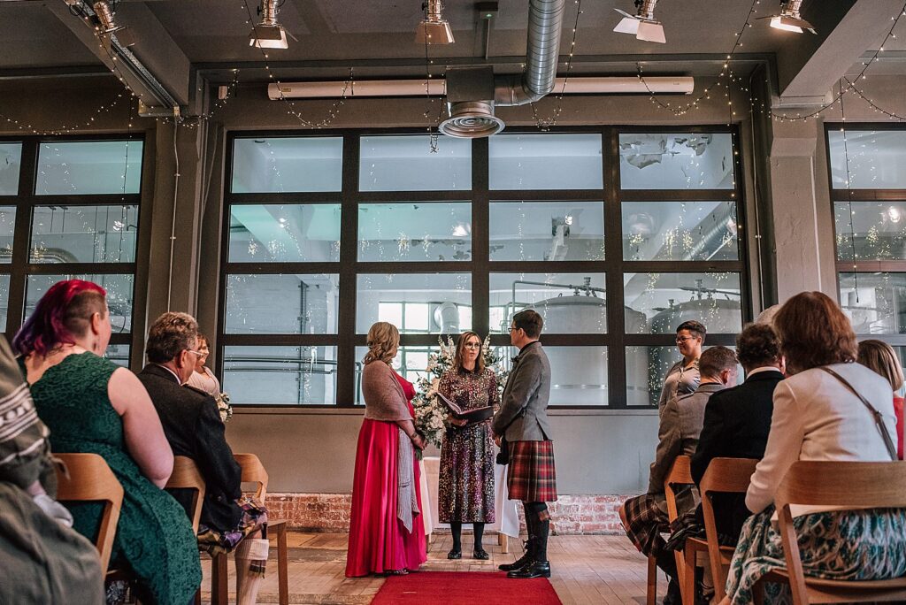 west brewery wedding ceremony with bride and groom standing with celebrant and seated guests inside west on the green overlooking glasgow brewery