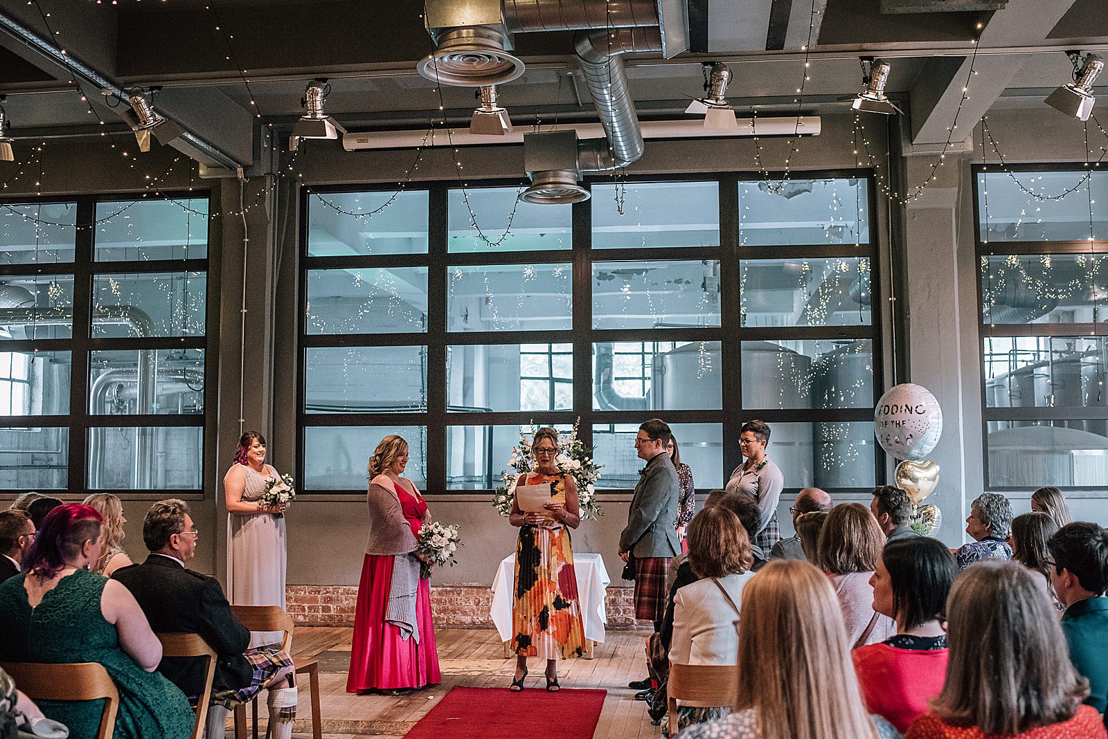 bride and groom standing with a family member for speech during their relaxed diy wedding at west brewery with balloons and fairy lights