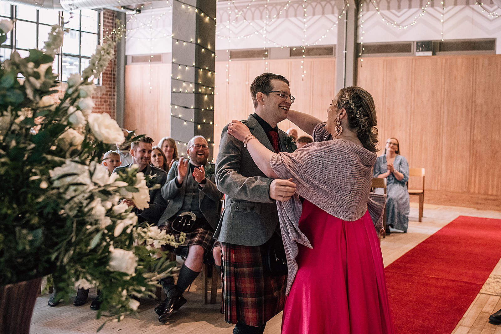 bride and groom hugging after getting married at west brewery wedding with guests cheering and bride dressed in pink wedding dress