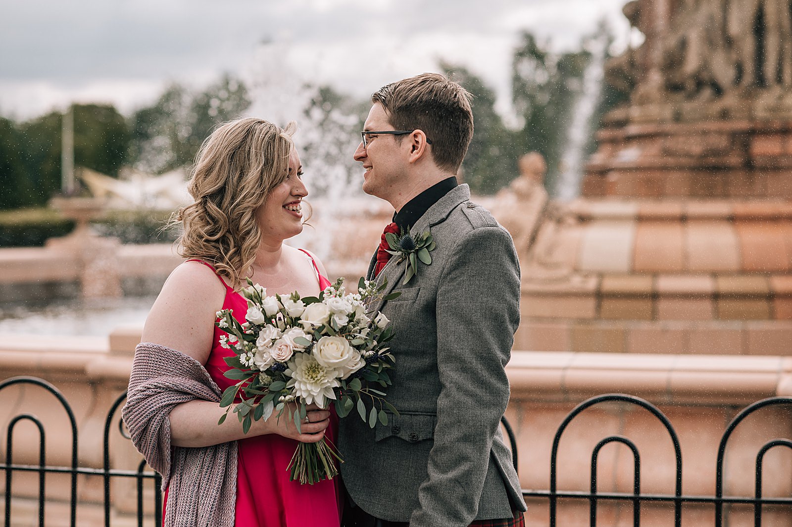 bride and groom looking at each other and smiling standing in front of fountain on glasgow green after their west brewery wedding