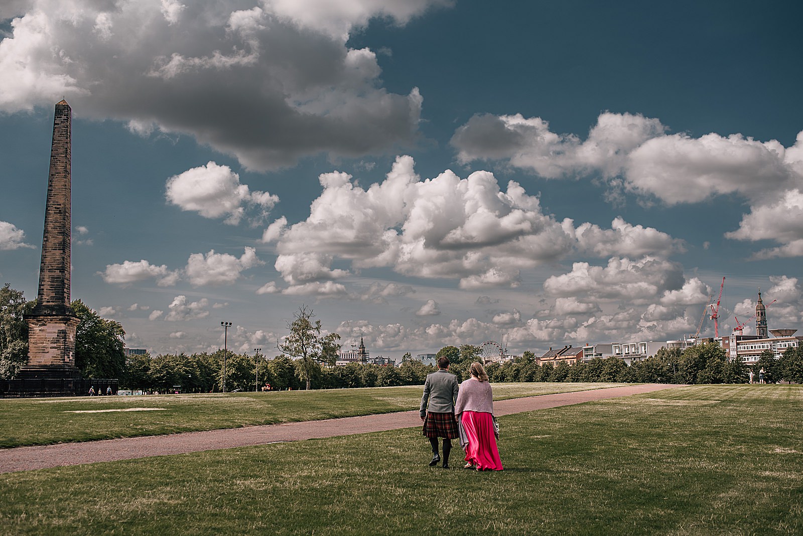 groom and bride in pink wedding dress walking across glasgow green on a sunny day after their west brewery wedding