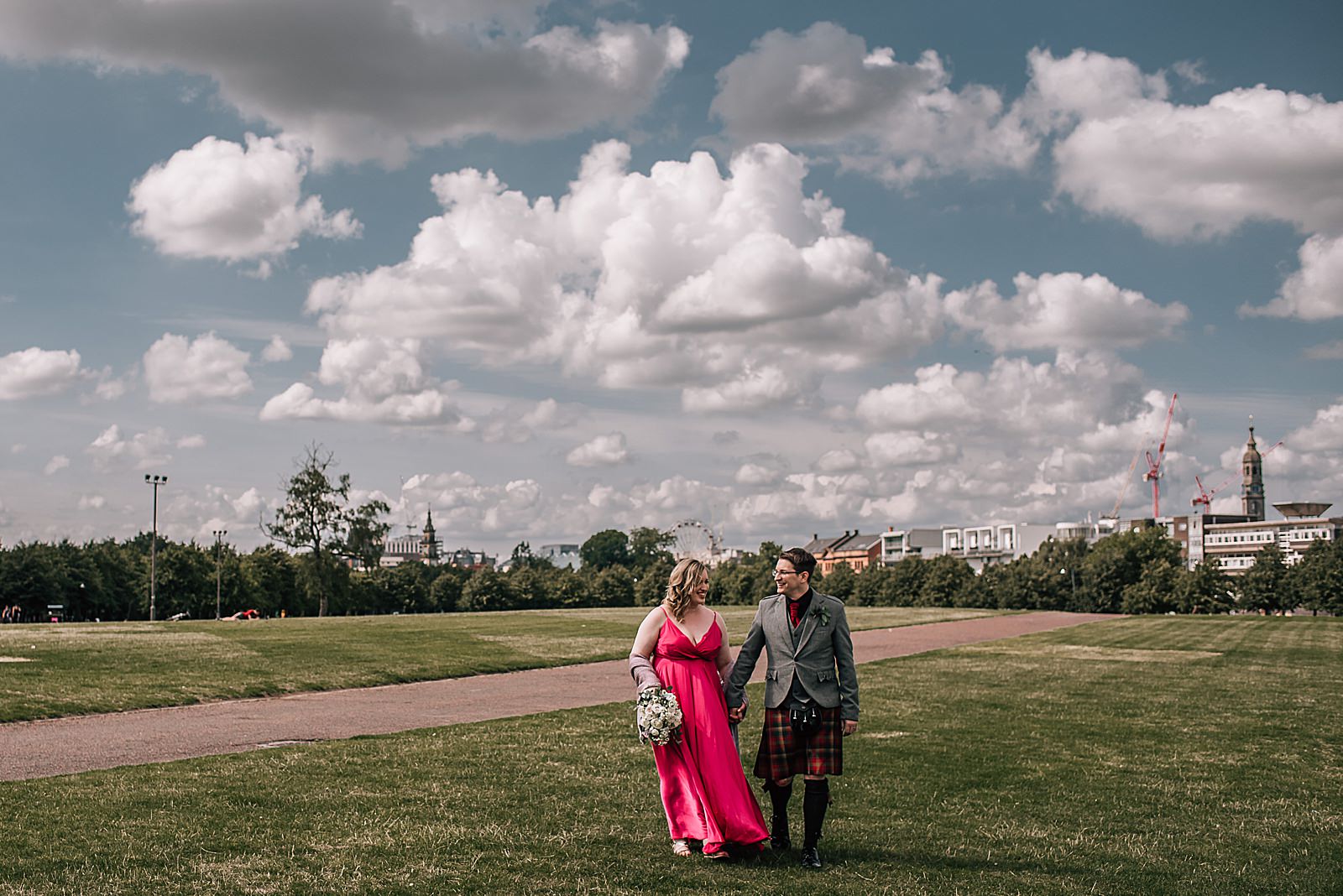 bride in pink wedding dress walking with her groom across glasgow green on a sunny day after their unique wedding glasgow at west brewery