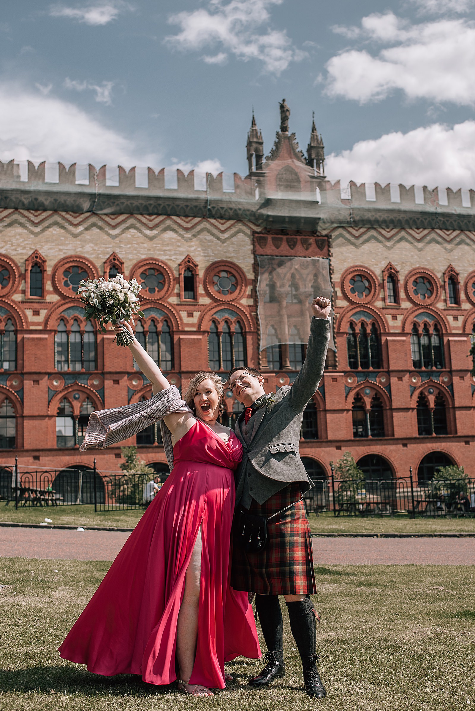 happy bride and groom punching the air after their west brewery wedding where they're standing outside in front of west brewery on glasgow green