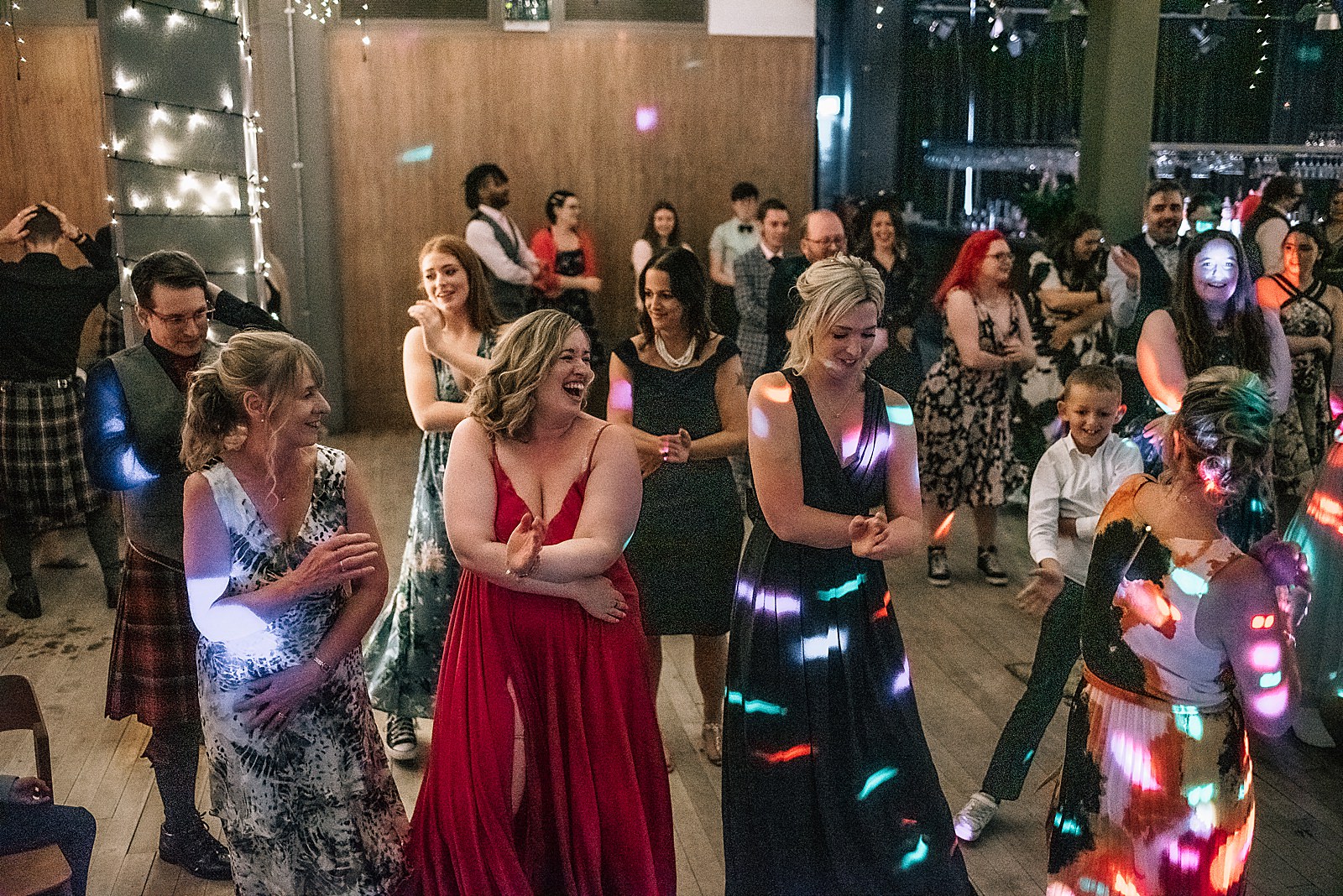 guests laughing and dancing at party during west brewery wedding with coloured lights