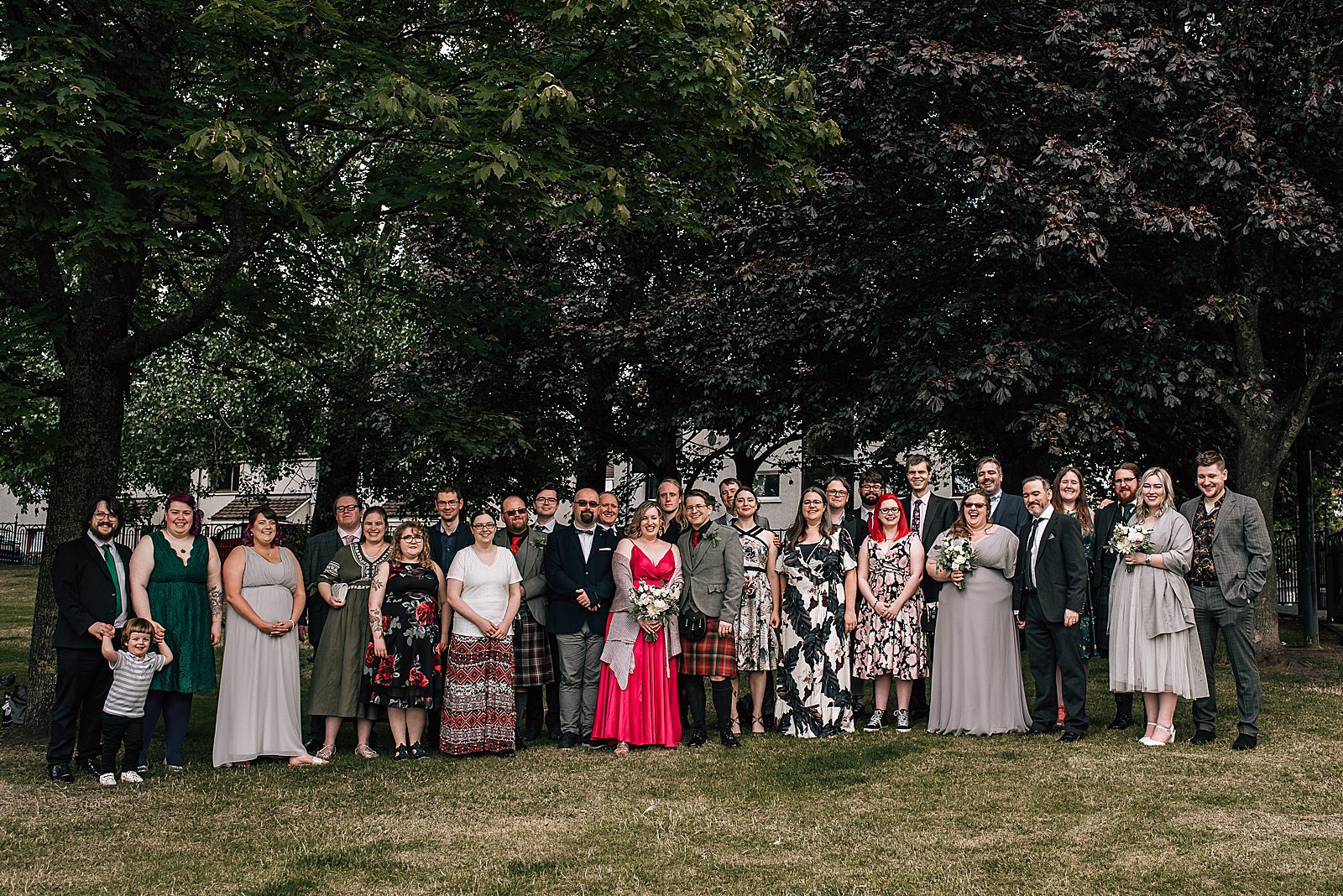 lots of wedding guests standing on glasgow green for picture by alternative wedding photographer glasgow during small wedding glasgow