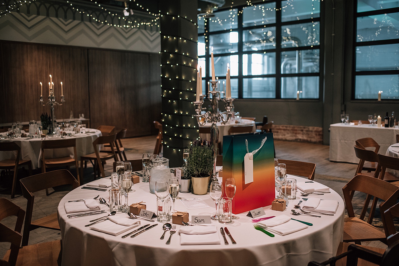 inside west brewery wedding reception with tables decorated with large silver candelabra and twinkling fairy lights
