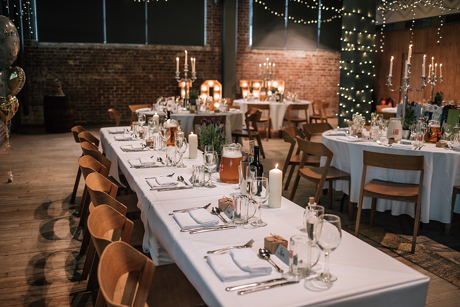 inside west brewery wedding reception with tables decorated with large silver candelabra and twinkling fairy lights brick walls and rustic florals