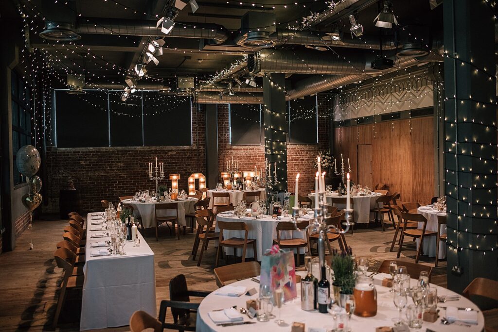 inside west brewery wedding reception with tables decorated with large silver candelabra and lots of twinkling fairy lights and balloons for unique wedding glasgow