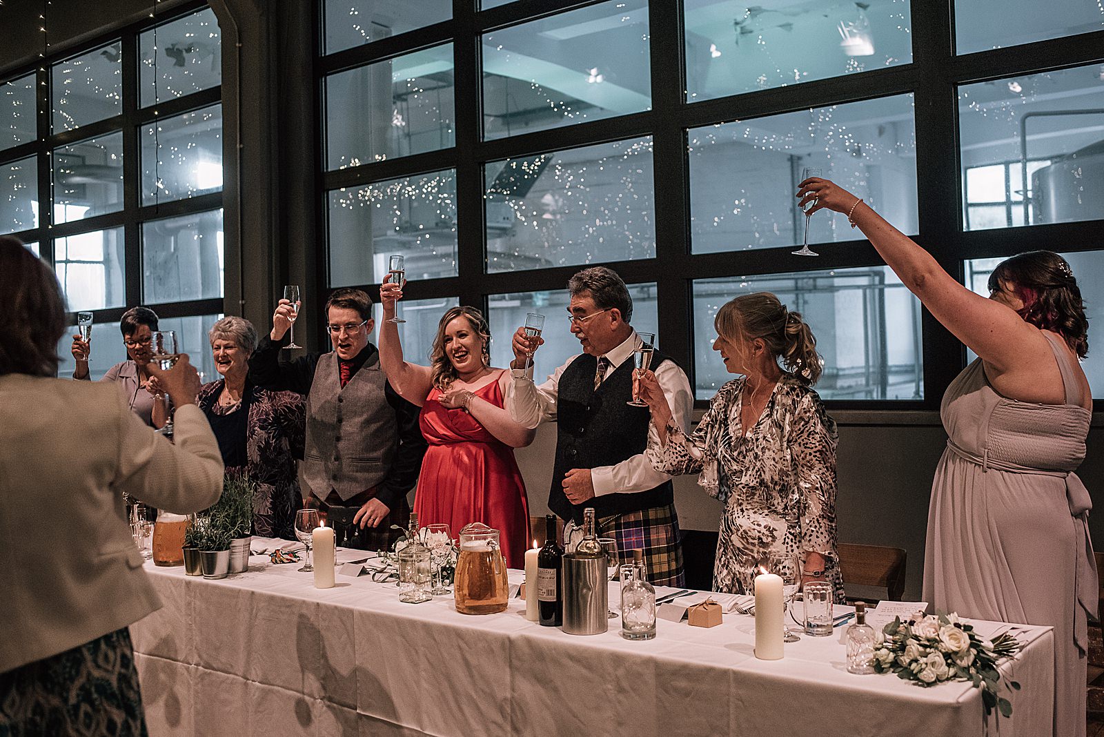 top table cheers at west brewery wedding after speeches in front of big window showing the west brewery