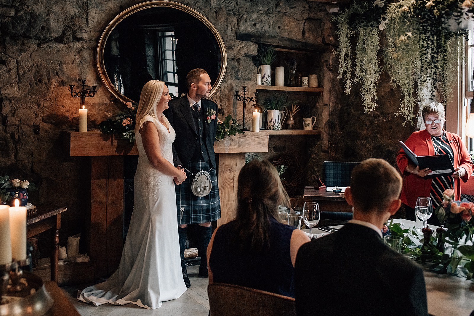 bride and groom standing with celebrant during wedding ceremony in atmospheric cosy wedding venue in glasgow with foliage chandelier
