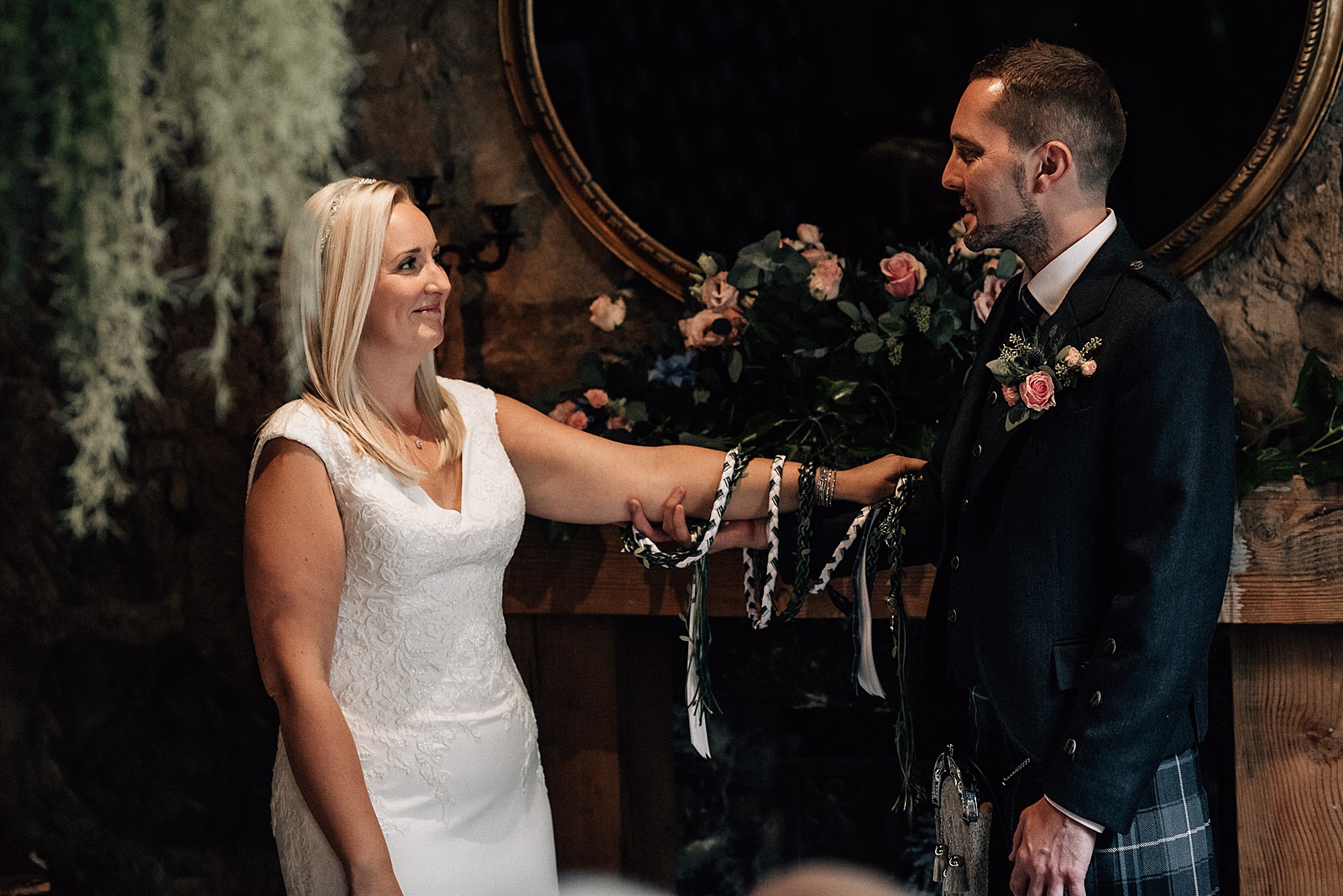 bride and groom smiling at each other during hand fasting ceremony at their the both glasgow wedding with beautiful pink and blue flower arrangement