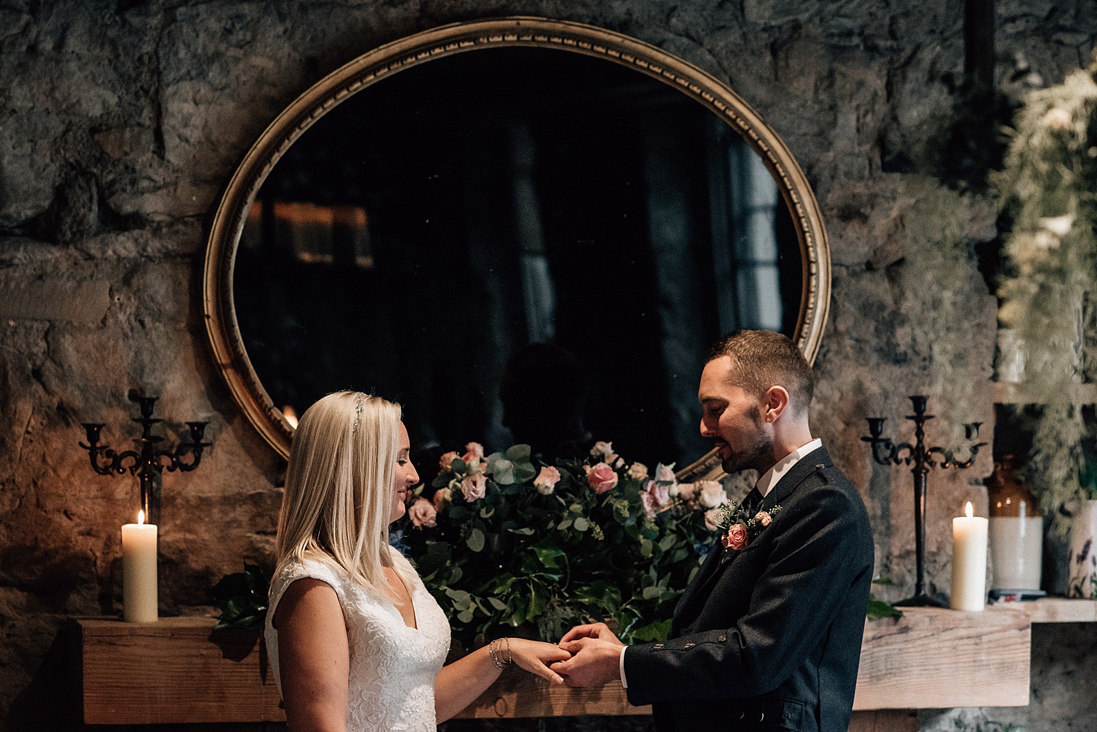 bride and groom exchanging wedding rings in front of beautiful oval mirror during their the bothy glasgow wedding which is a quirky glasgow wedding venue