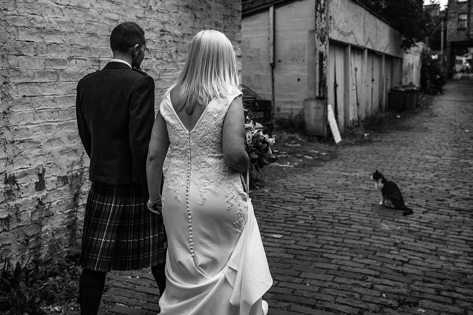 black and white photograph of bride and groom walking down cobble stone street in glasgow after their ceremony at the bothy glasgow wedding