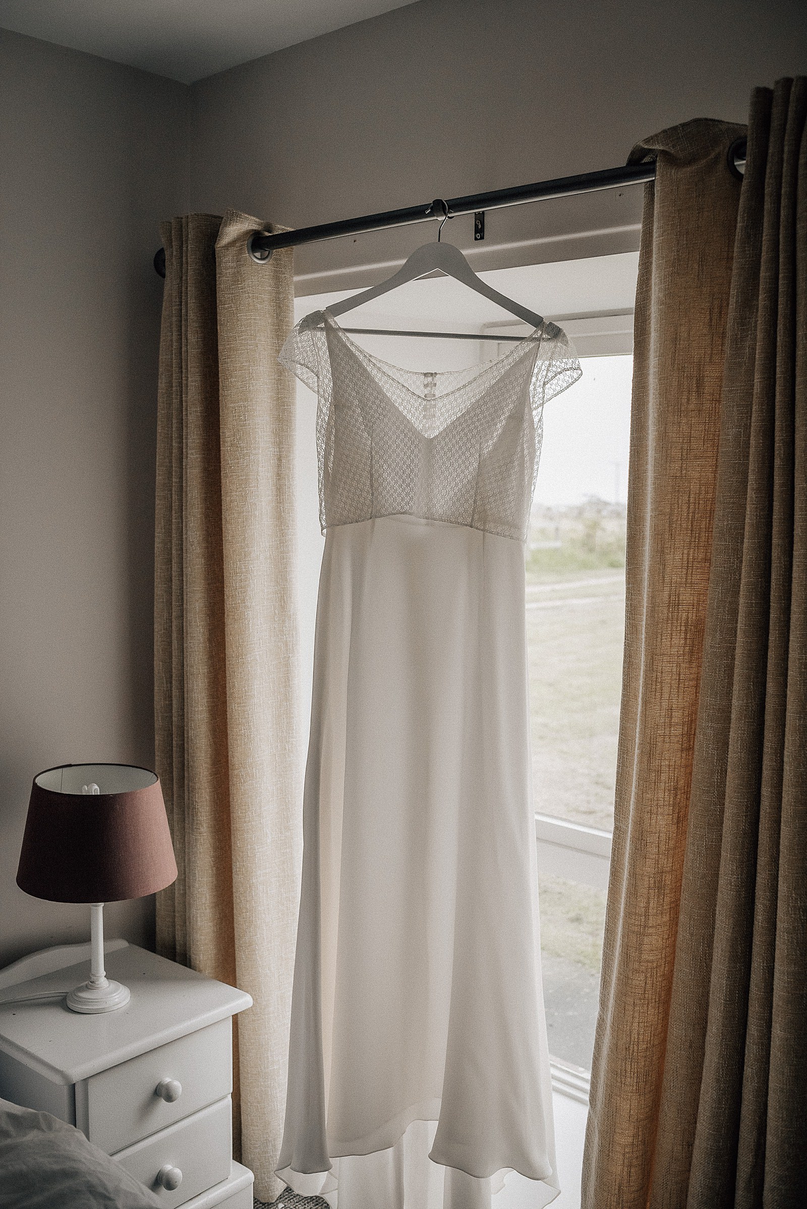 beautiful flowy white boho wedding dress hanging in window at bridal party accommodation near the cow shed scotland