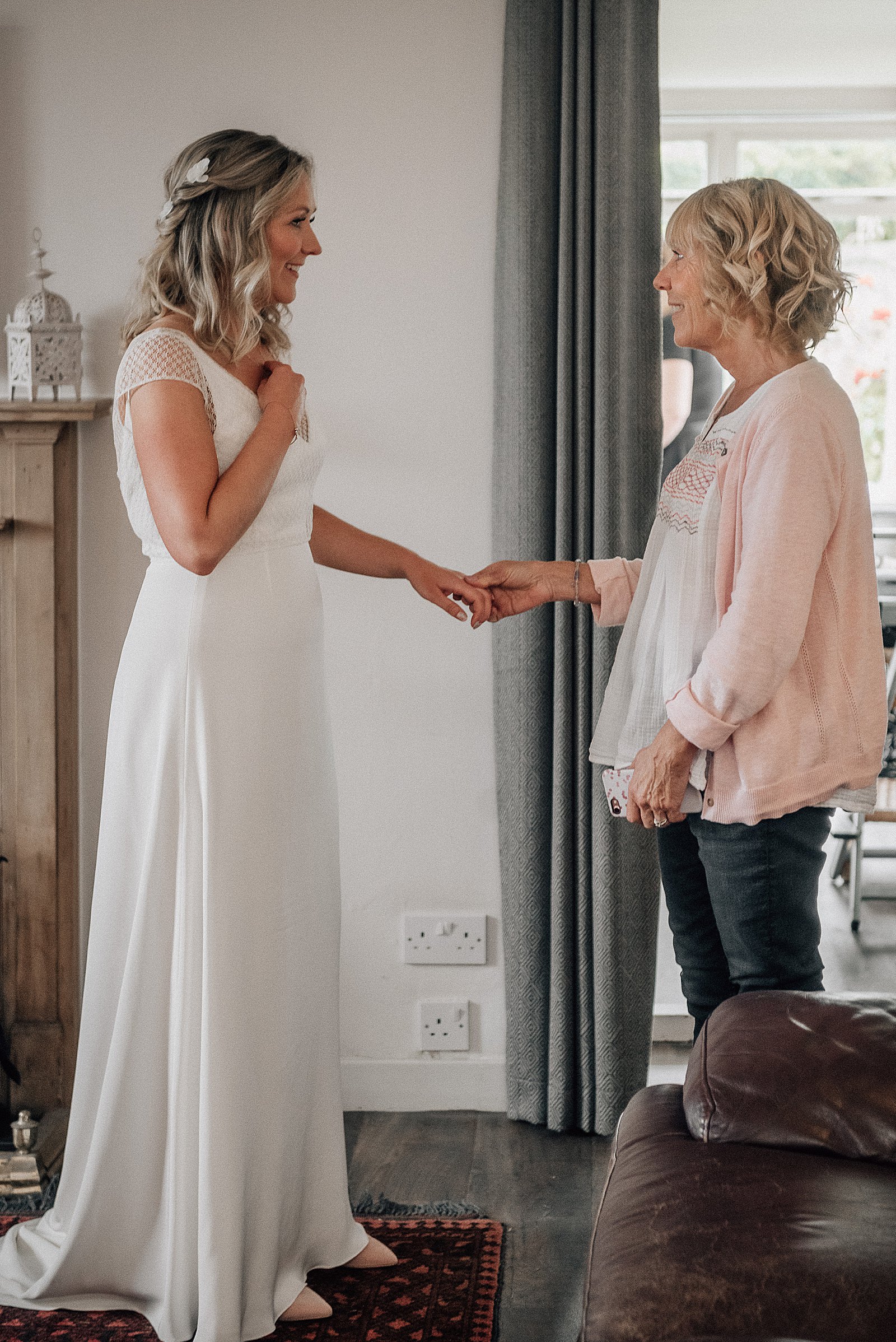 bride and mother's first look on wedding morning whilst holding hands and smiling inside bridal party accommodation at the cow shed scotland