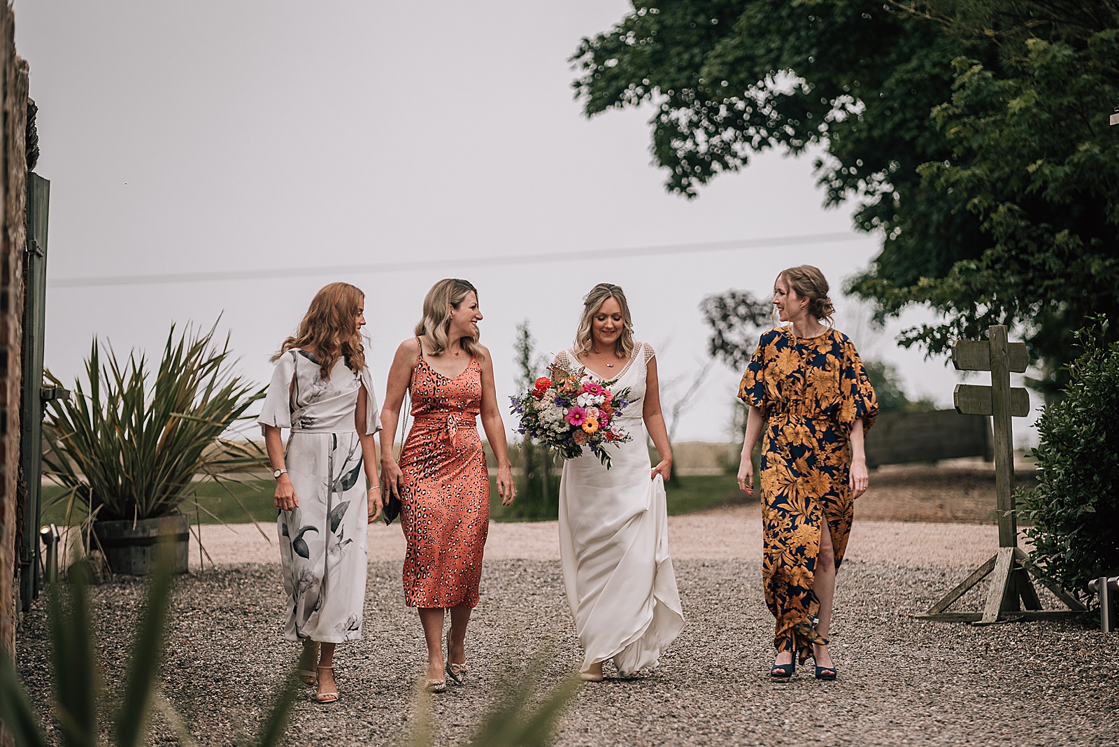 bride and bridesmaids walking to her wedding ceremony at the cow shed scotland dressed in colourful summer dresses and smiling