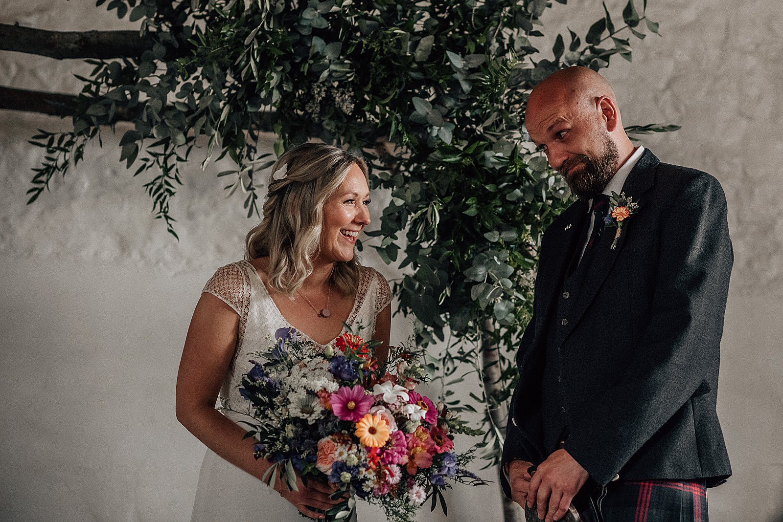 bride laughing with groom holding her brightly coloured bouquet inside barn at the cow shed scotland