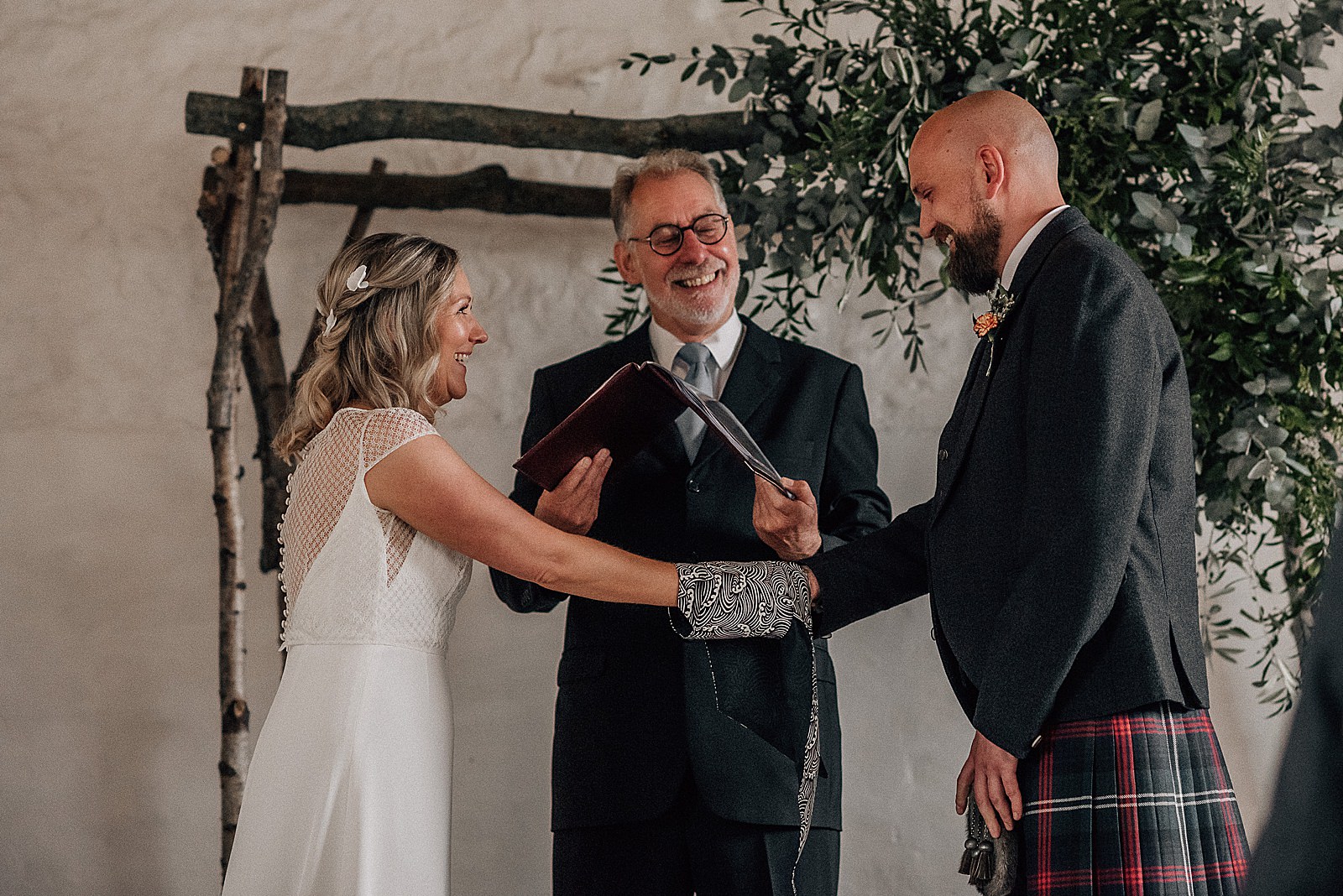 bride and groom smiling in front of celebrant during hand fasting ceremony at their barn wedding at the cow shed scotland