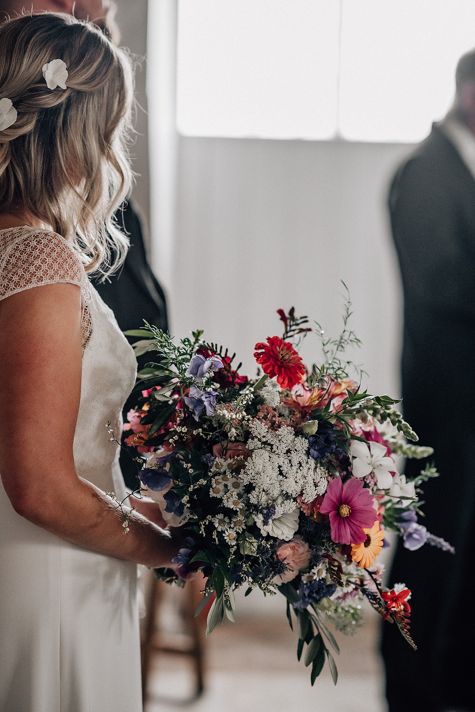 bride holding her beautiful bouquet of wild flowers in bright colours of red, pinks, purples, oranges and white during her wedding at the cow shed scotland