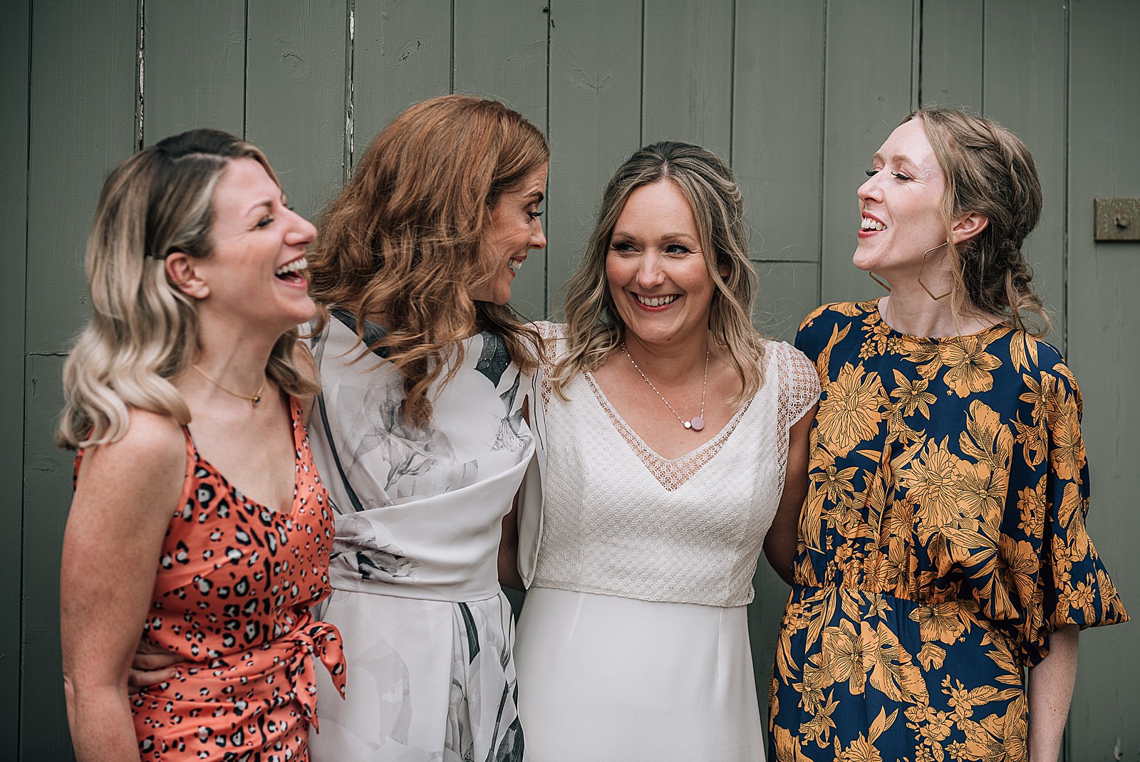 bride smiling and hugging her bridesmaids in front of green barn door at rustic barn wedding scotland