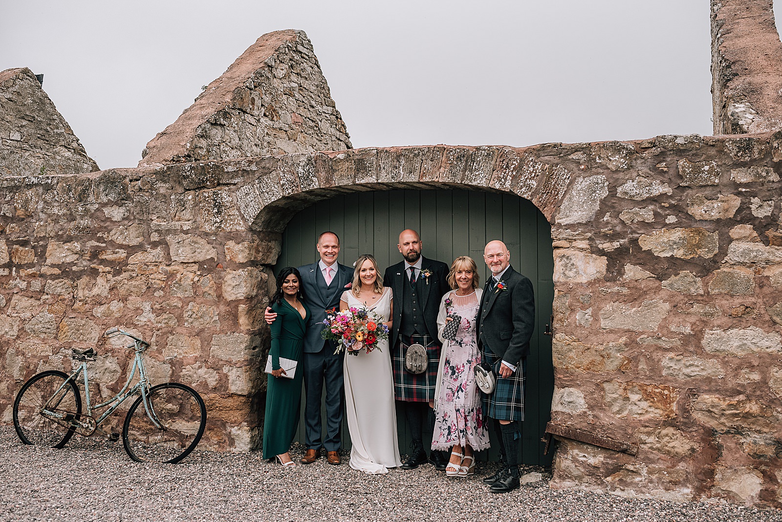 bride and groom with posing with family in barn door arch way in rustic farm wall during their wedding at the cow shed scotland