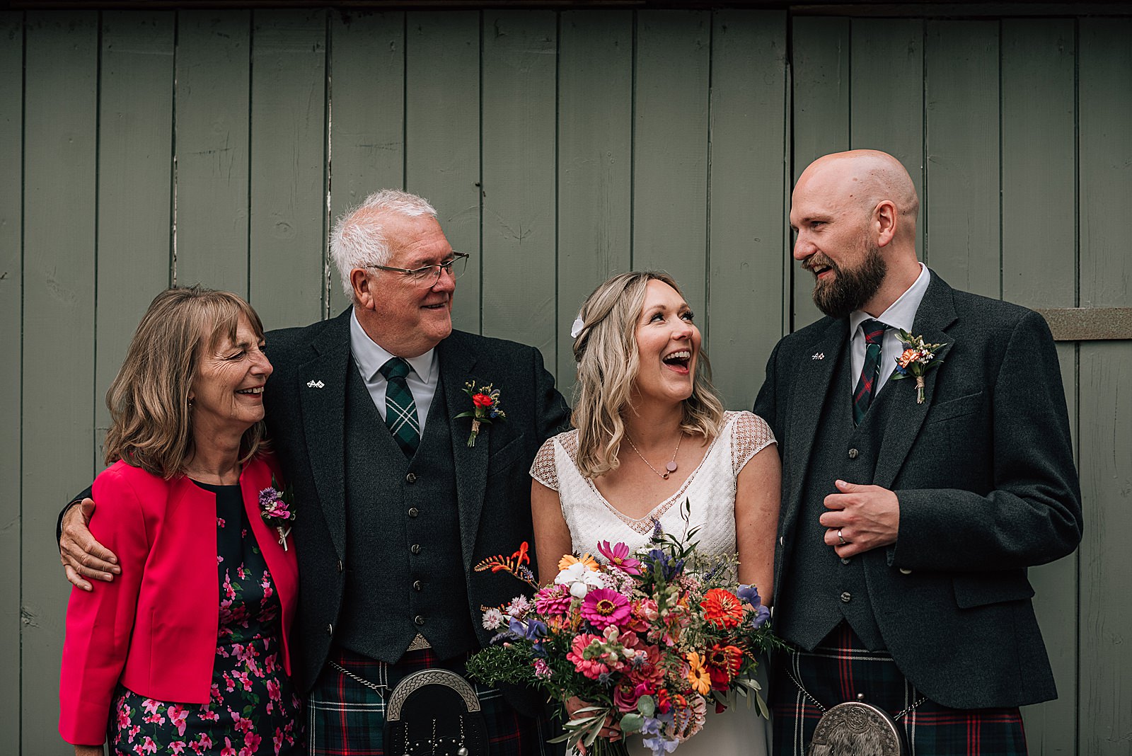 bride and groom laughing with family for a portrait in front of green barn door after their wedding ceremony at the cow shed scotland