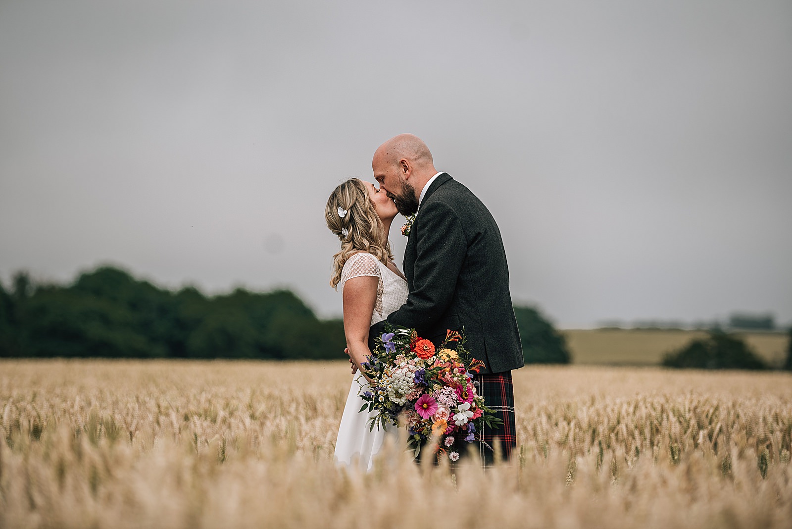 bride and groom kissing standing in wheat field at the cow shed scotland after their quirky Scottish wedding