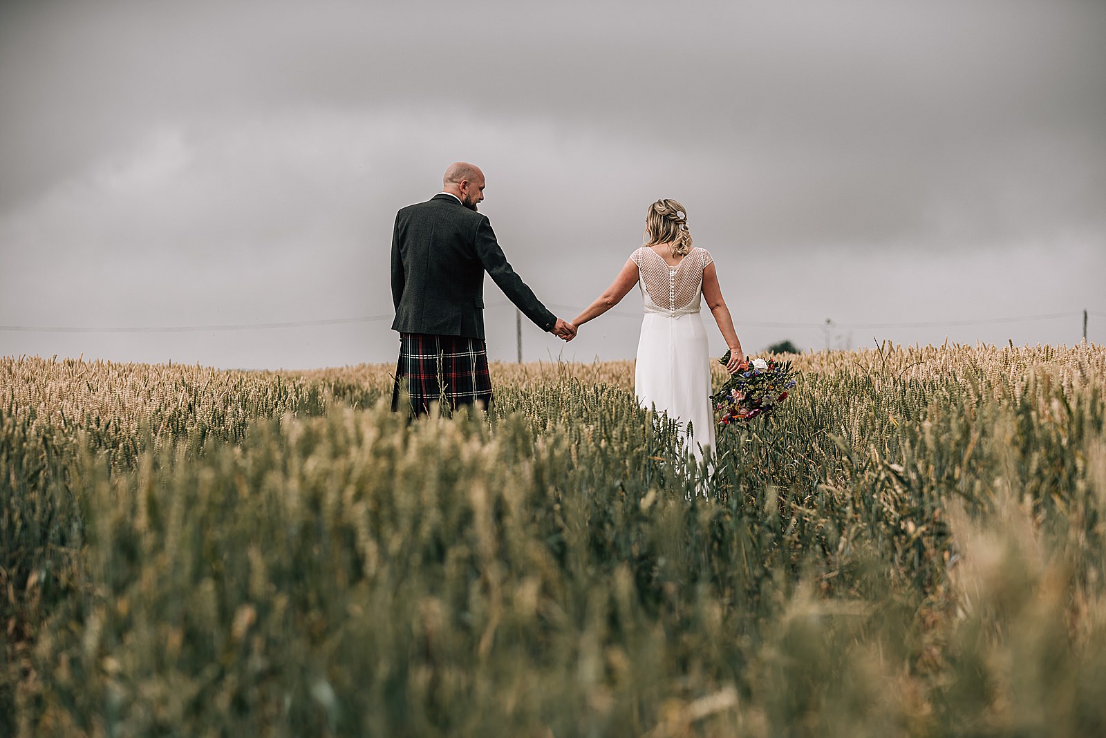bride and groom walking in wheat field on a sunny day at a wedding venue in St Andrews called the cow shed scotland
