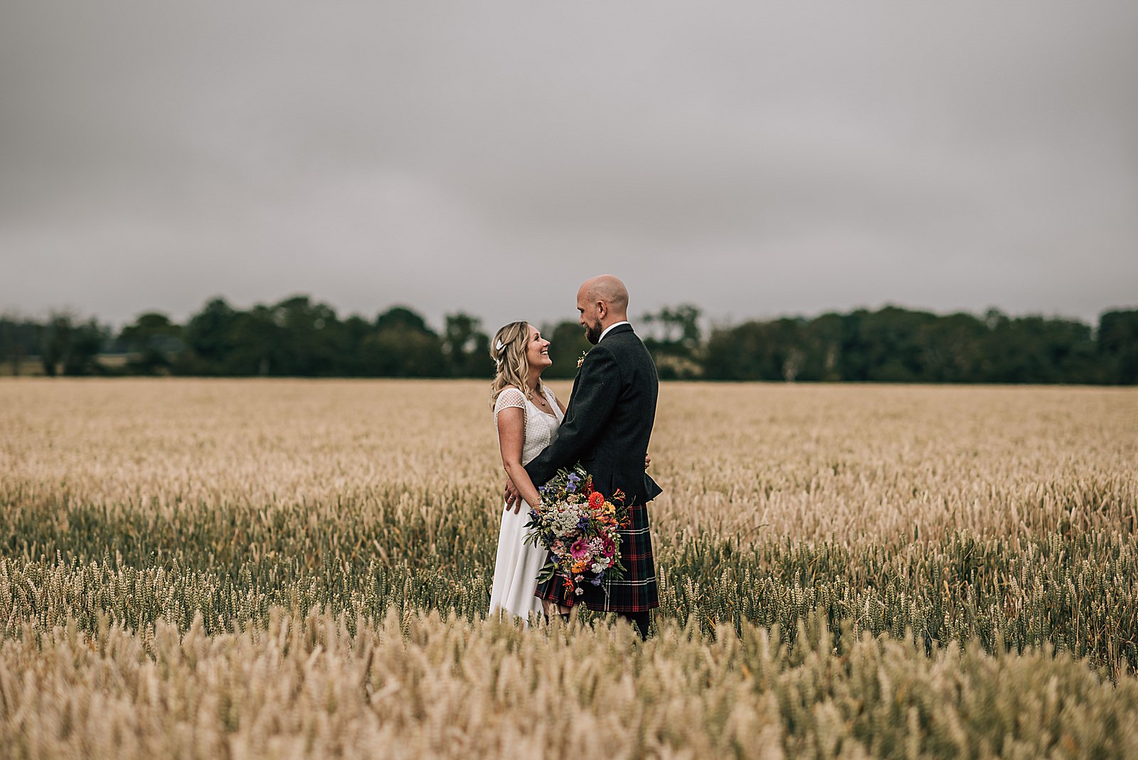 bride and groom hugging and smiling while standing in a wheat field during their wedding at the cow shed scotland