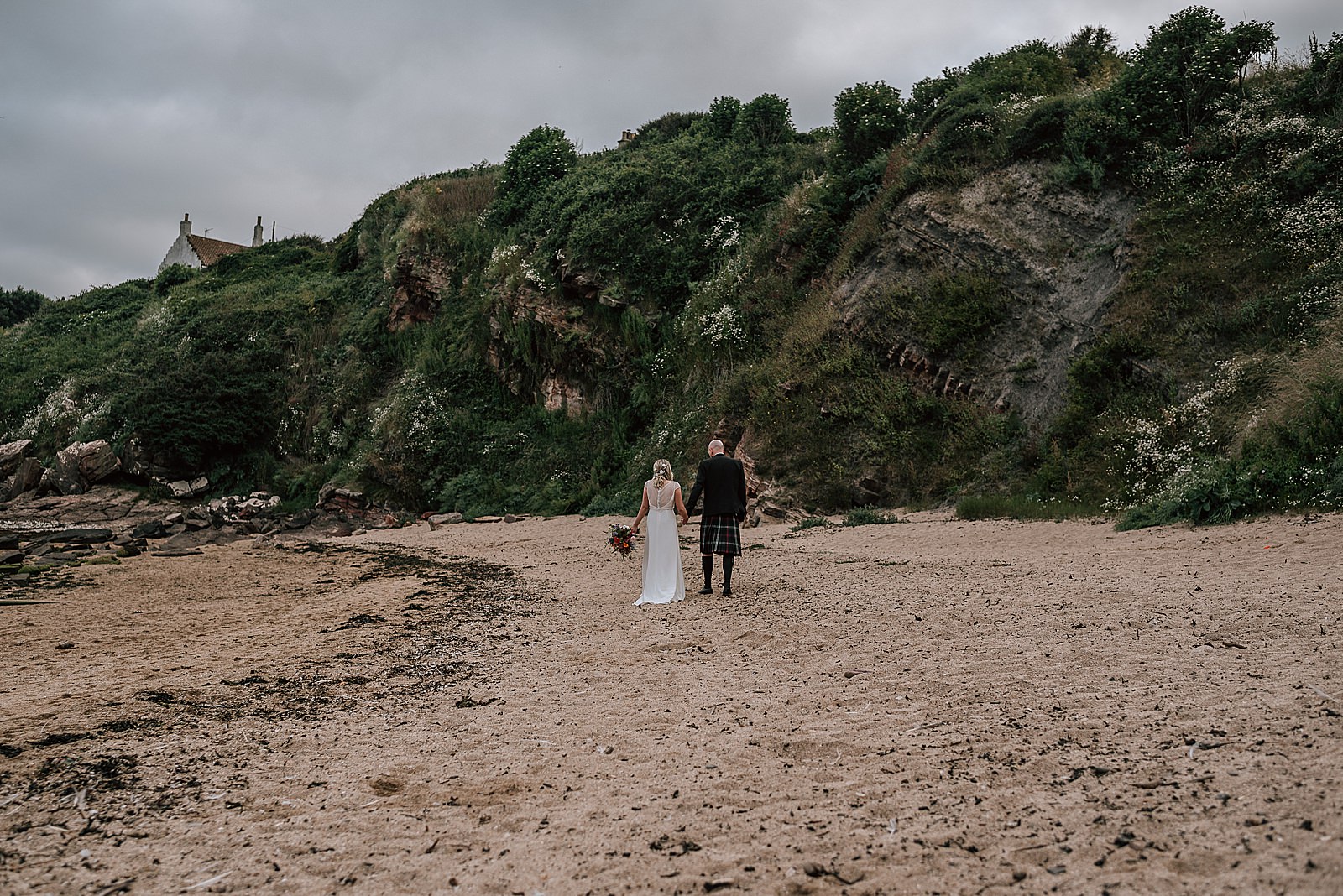 bride and groom walking along the beach near the cow shed scotland during their wedding at a quirky Scottish wedding venue in st andrews