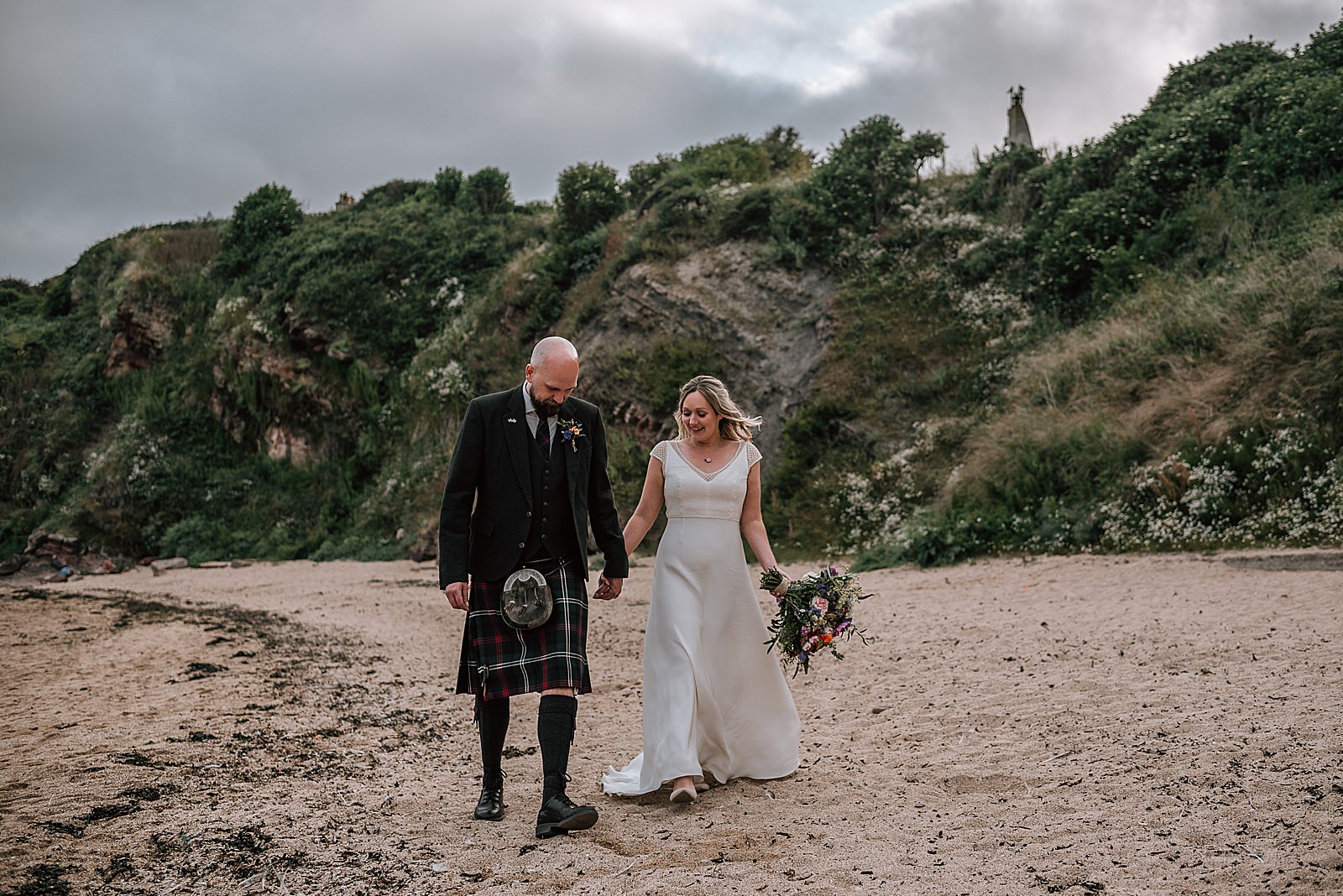 bride and groom walking along the beach near the cow shed scotland during their wedding at a diy Scottish wedding