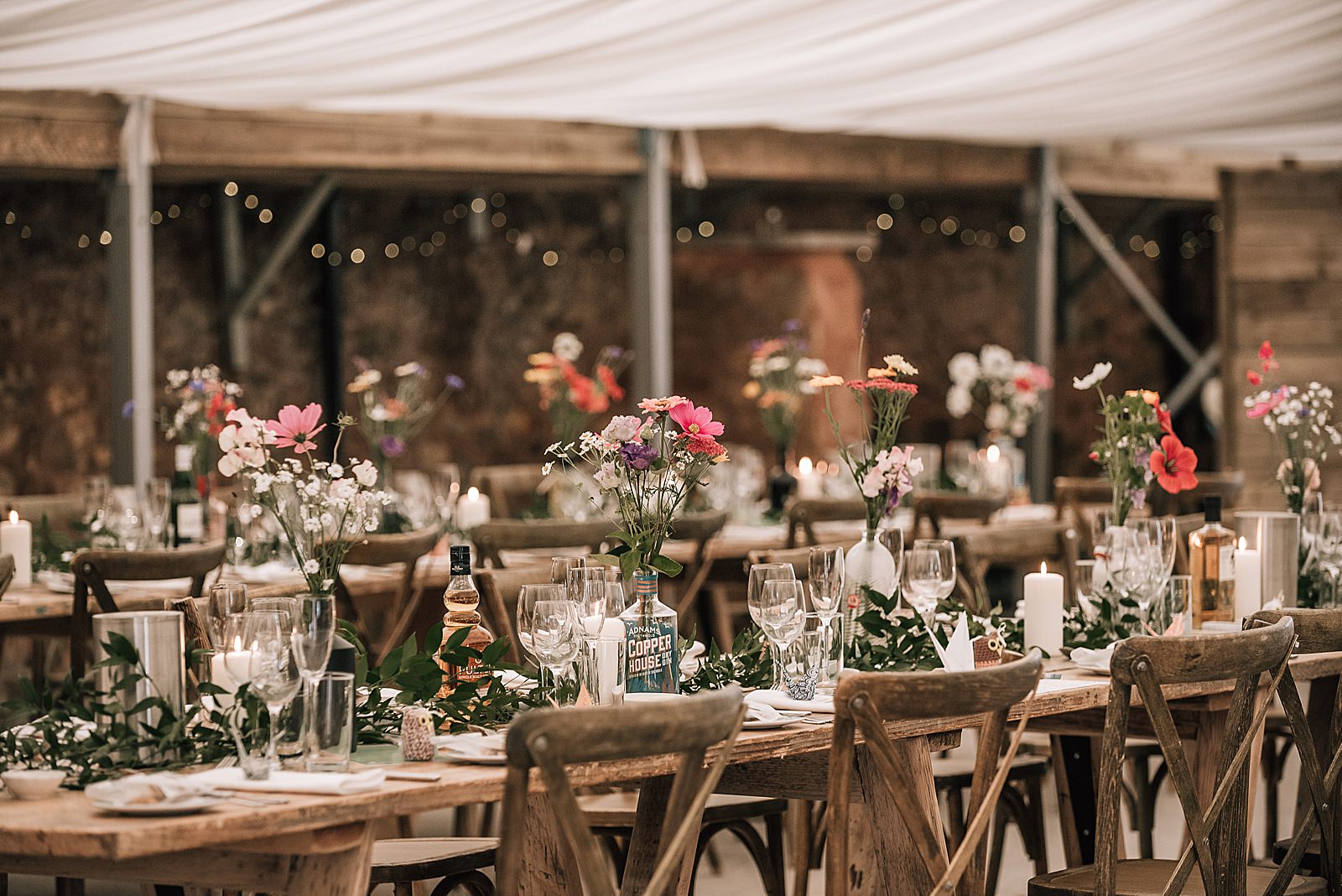 rustic wooden tables set with glassware, place settings and beautiful flowers for wedding at the cow shed scotland in barn in St Andrews at diy Scottish wedding