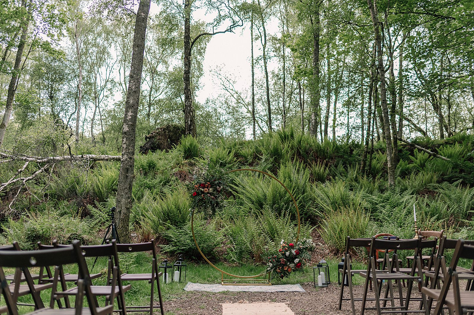 outdoor comrie croft wedding ceremony in woodland on sunny day with circular flower arch lanterns and rug