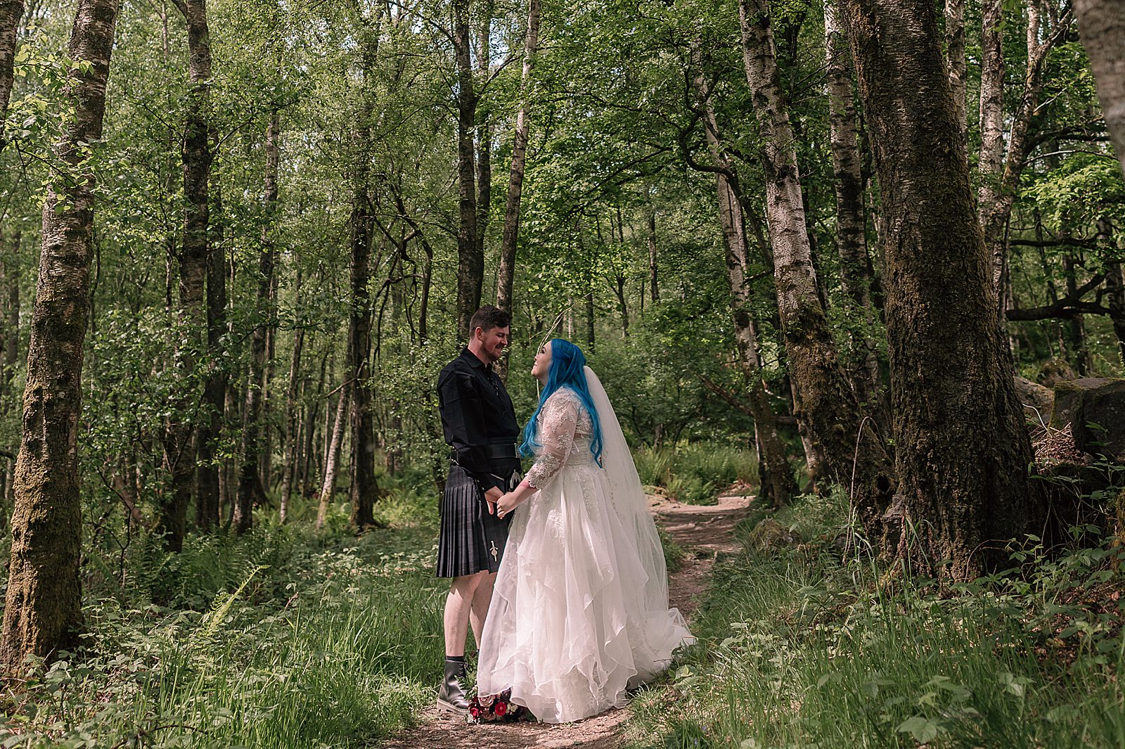 bride and groom looking at each other and smiling while standing in a green woodland on a sunny day at comrie croft wedding