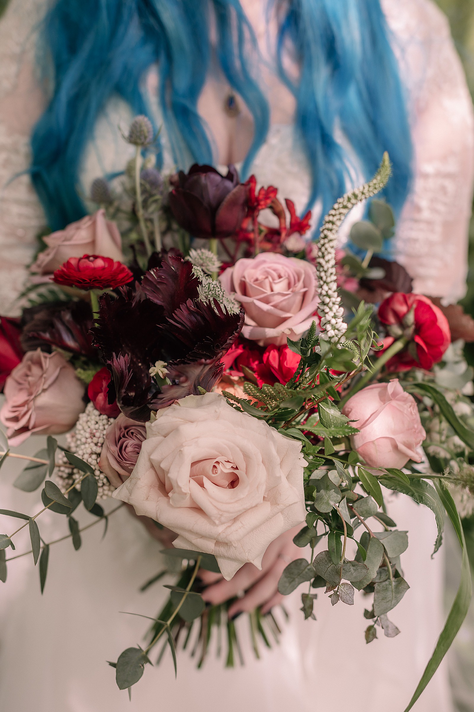 bride with blue hair holding a bouquet of dark purple pink and red flowers for her gothic wedding at Comrie Croft